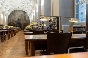 Interior de la Torre Astronómica del Clementinum y la Biblioteca Barroca con largas mesas de madera, sillas y estanterías bajo altos techos abovedados.