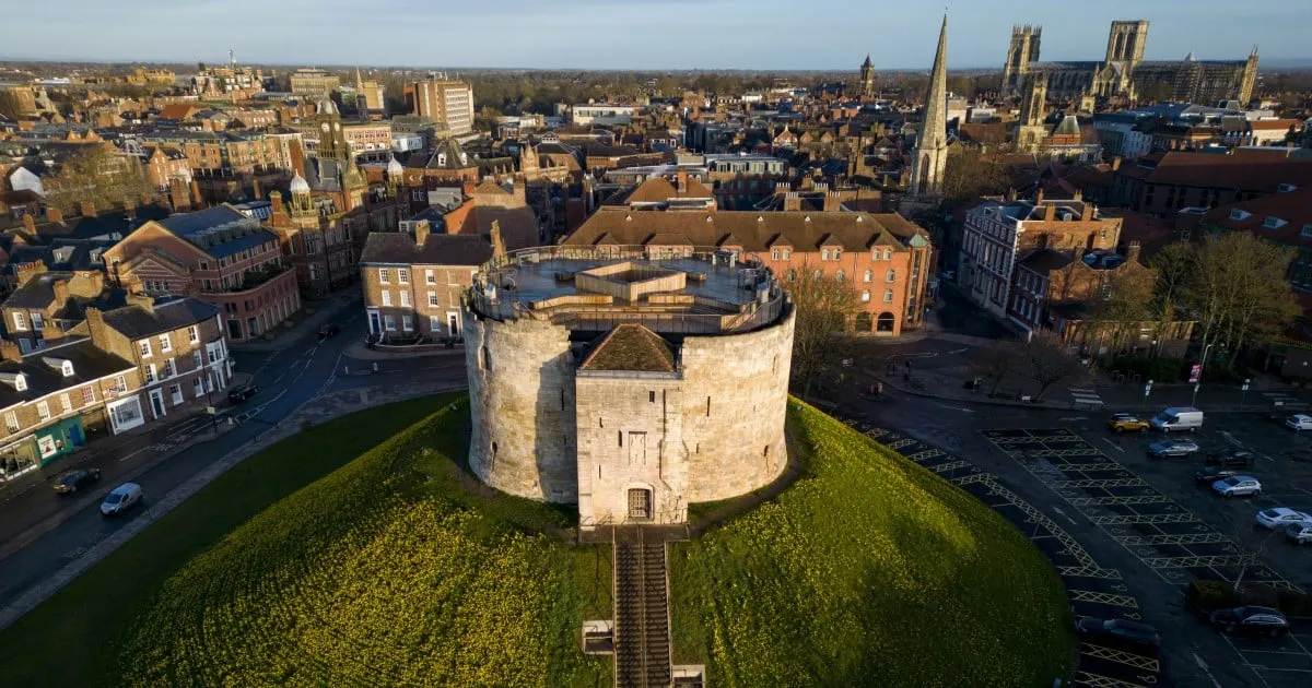 Widok z lotu ptaka na Clifford's Tower na trawiastym wzniesieniu, z miastem York i katedrą York Minster w tle.