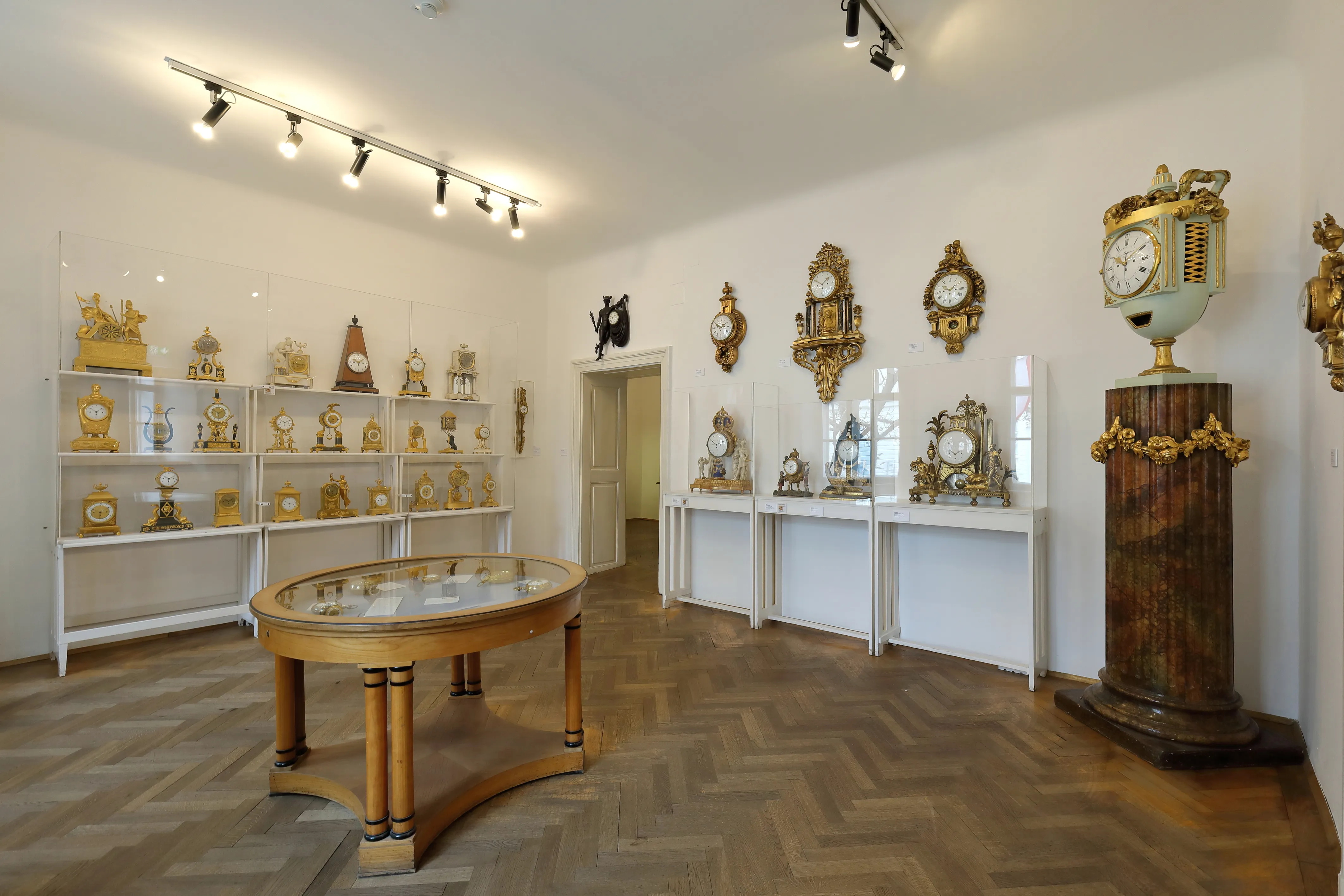 Interior of the Clock Museum with display shelves of clocks, a central table, and a large clock on a pedestal