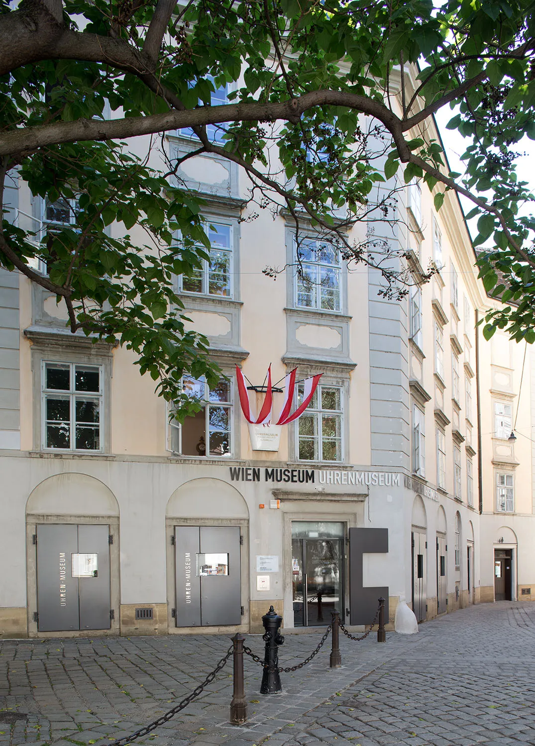 El exterior del edificio del Wien Museum Uhrenmuseum con un cartel sobre la entrada y una cinta roja y blanca colgando de la fachada.