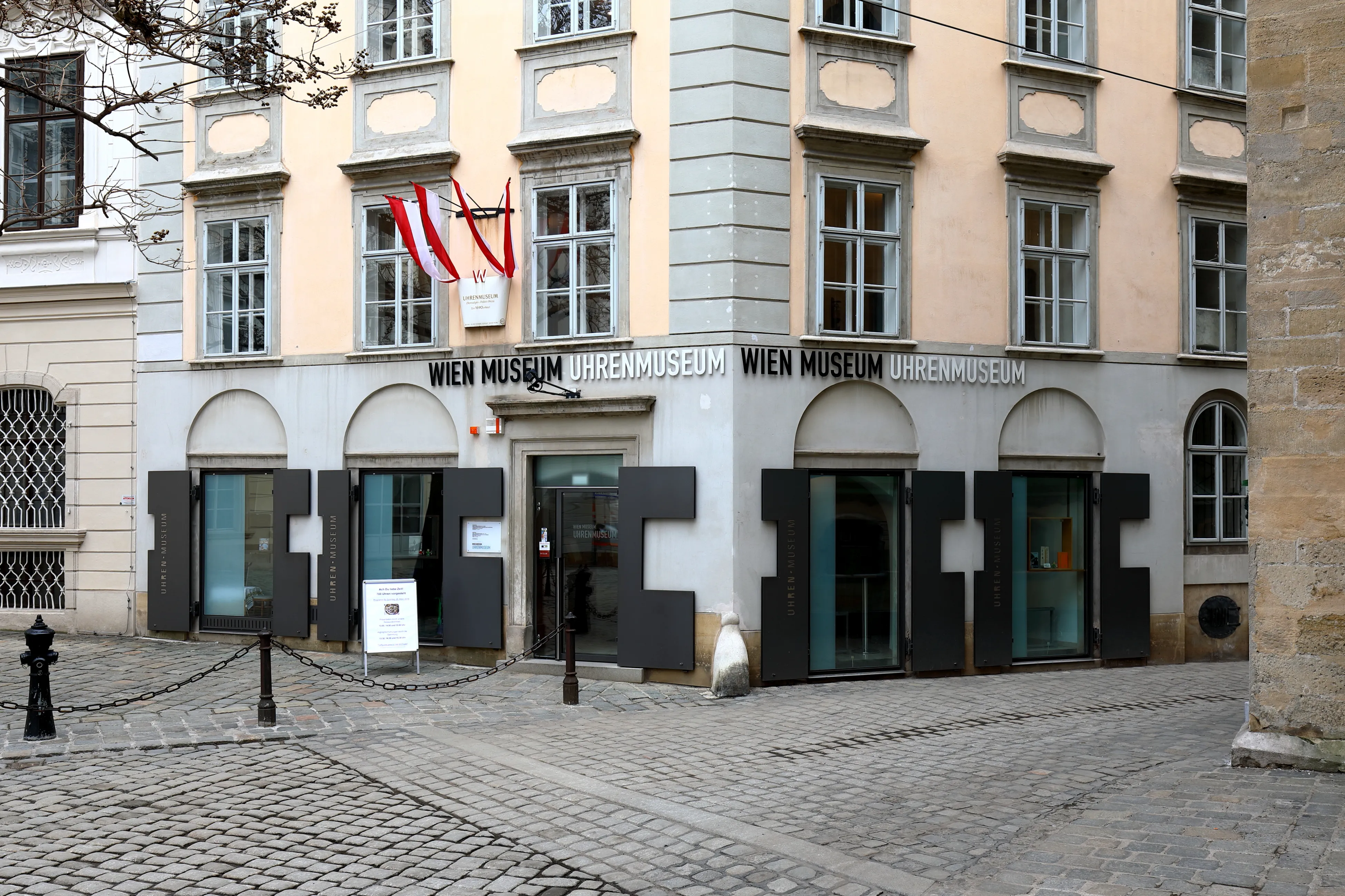 El exterior del Wien Museum Uhrenmuseum con su nombre visible en la fachada y una bandera sobre la entrada