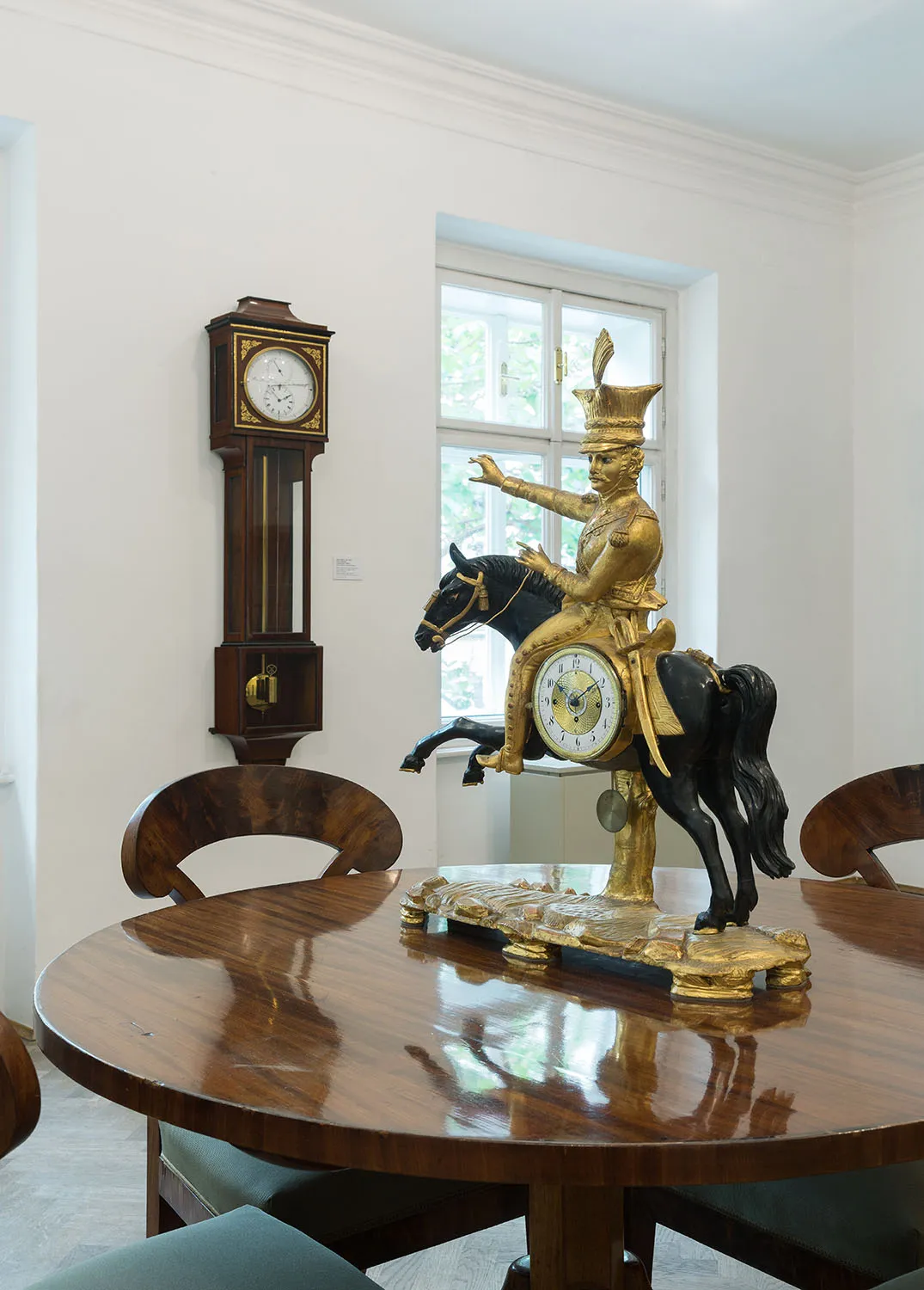 Una escultura de reloj dorada de una figura a caballo y un reloj de pie de madera expuestos en una sala de museo