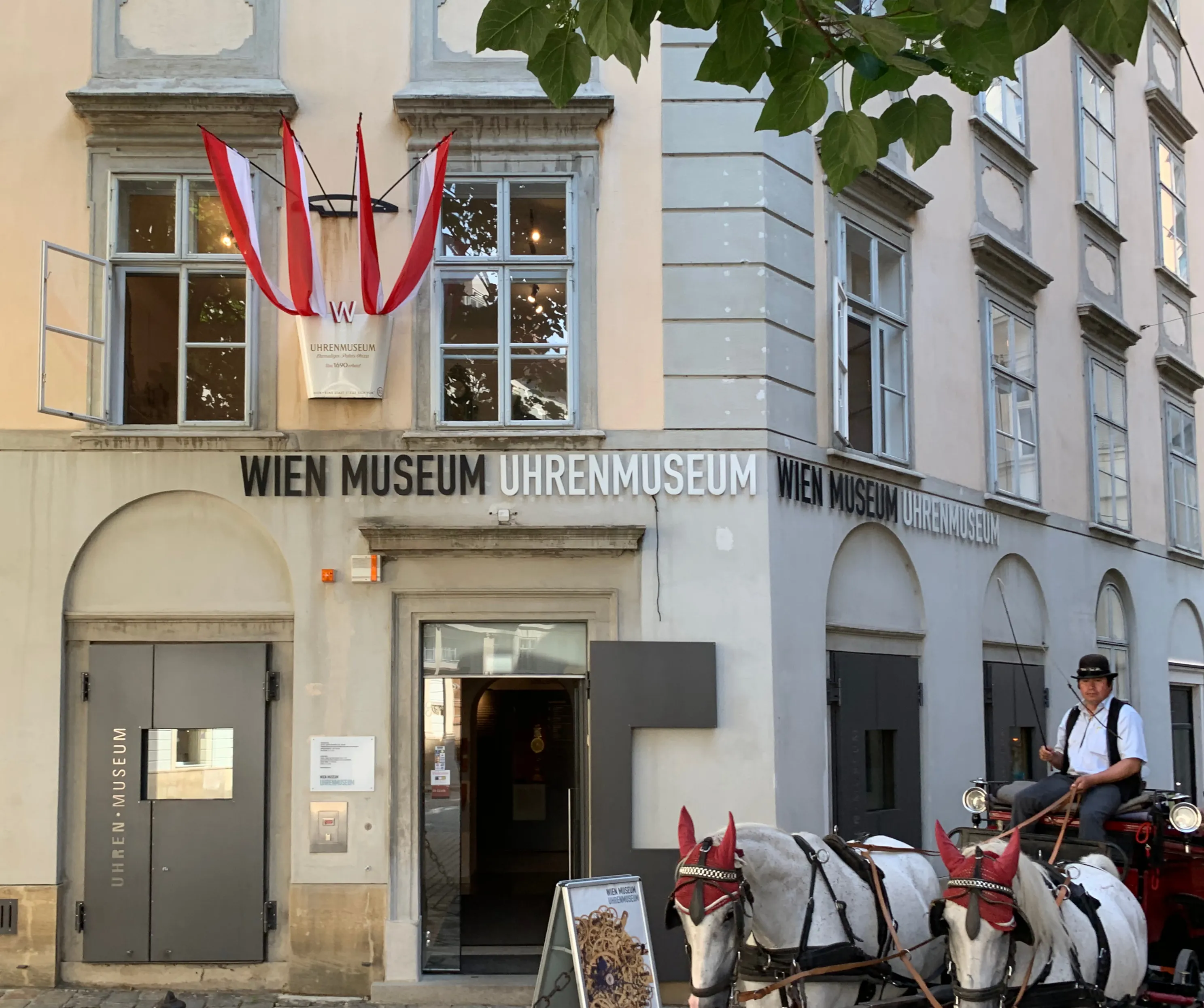 The entrance to the Wien Museum Uhrenmuseum with a horse-drawn carriage in front of the building.