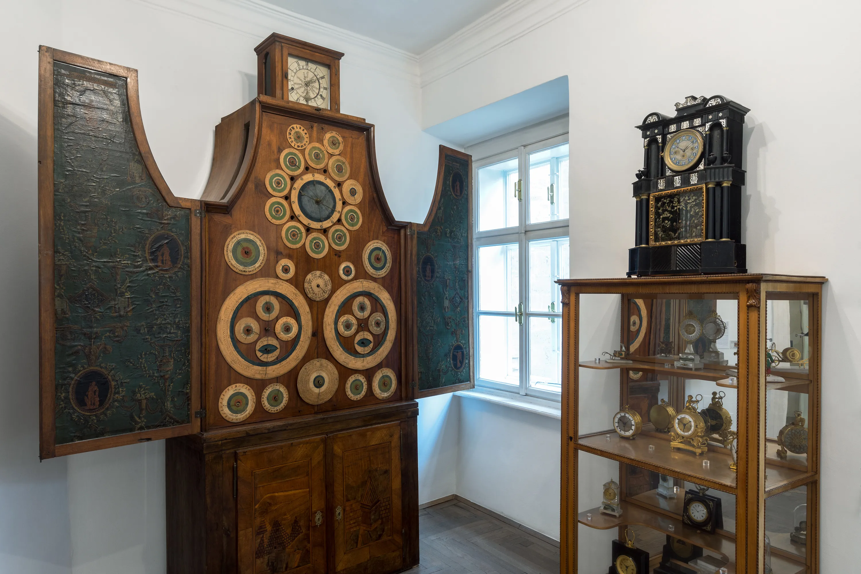 Un gran armario de madera para relojes con esferas circulares y una vitrina de cristal con relojes en una sala de museo