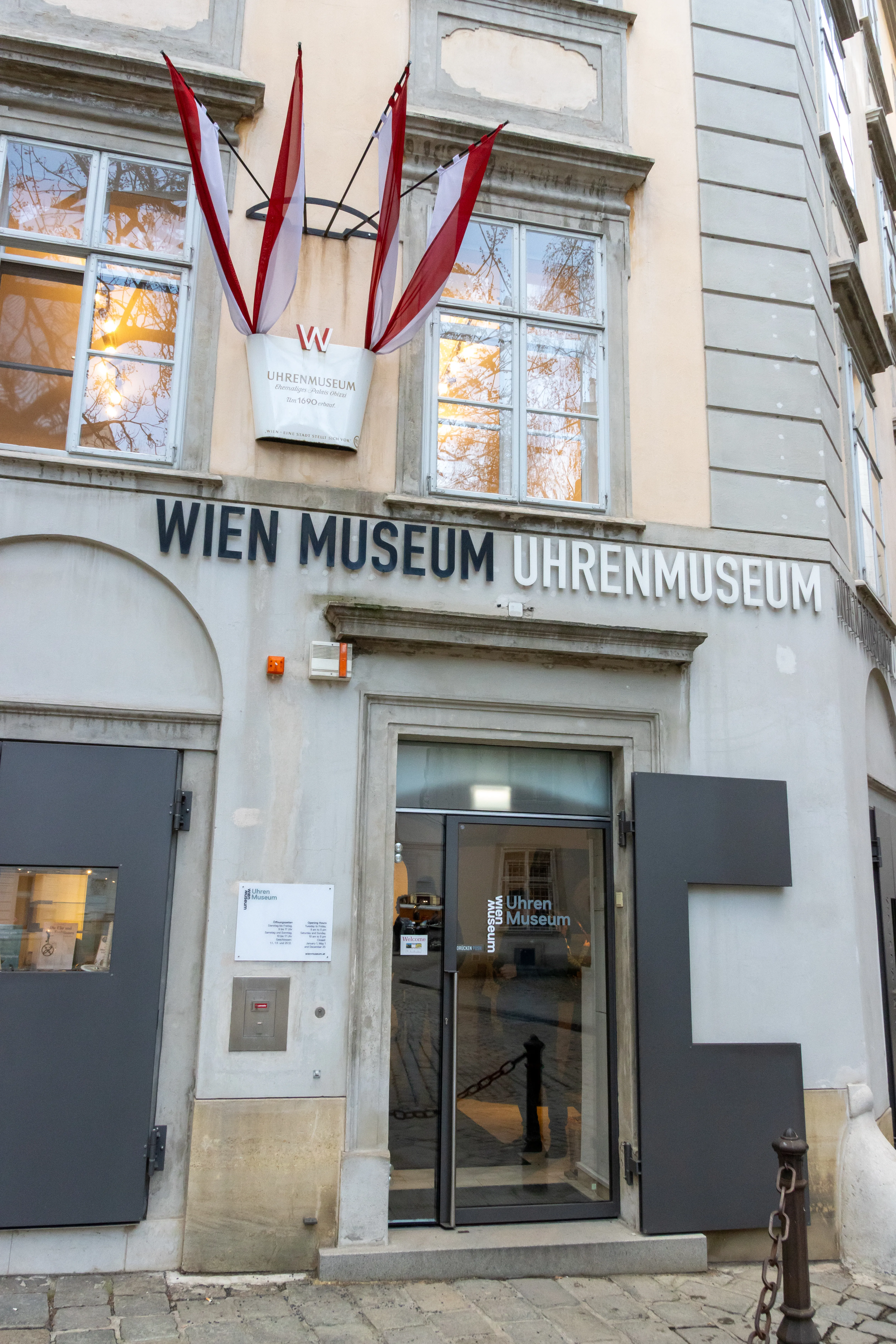 Entrada al Wien Museum Uhrenmuseum con letrero y banderas en la fachada de un edificio