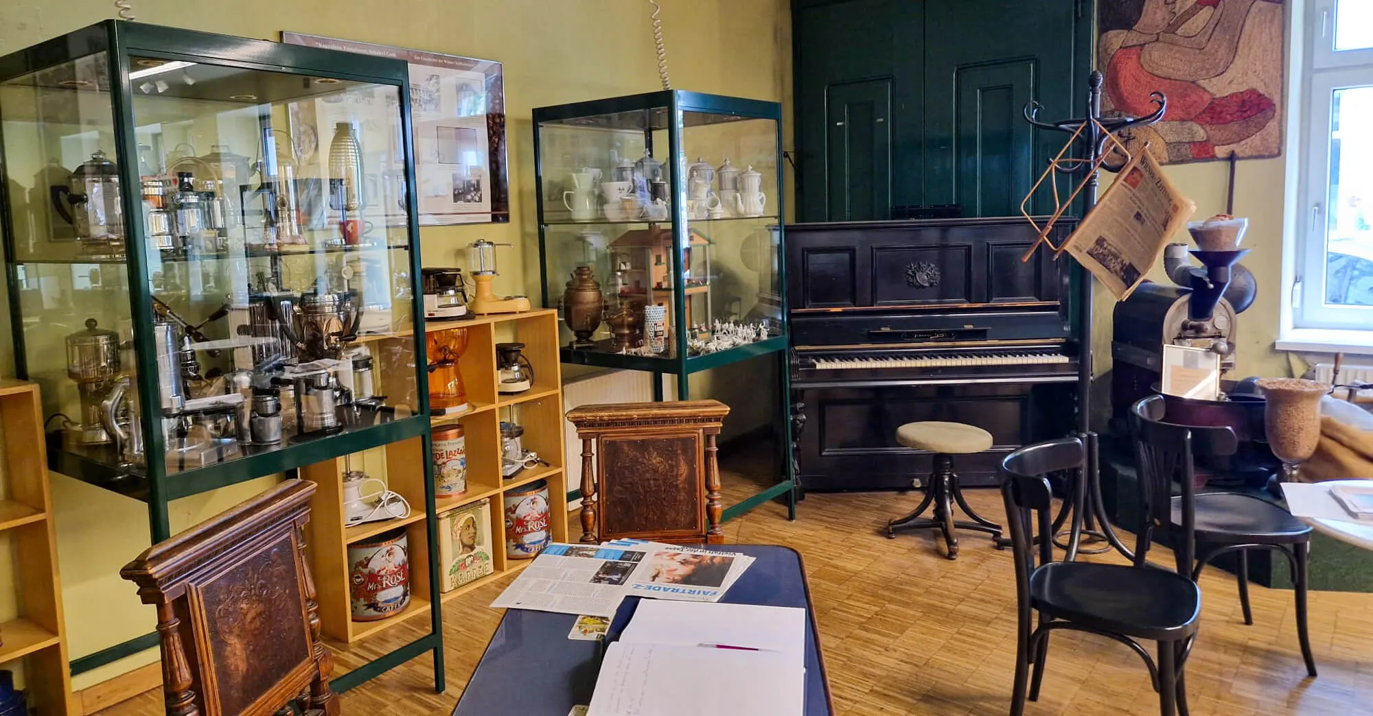 Interieur van het Koffiemuseum met glazen vitrines, een piano en houten meubilair