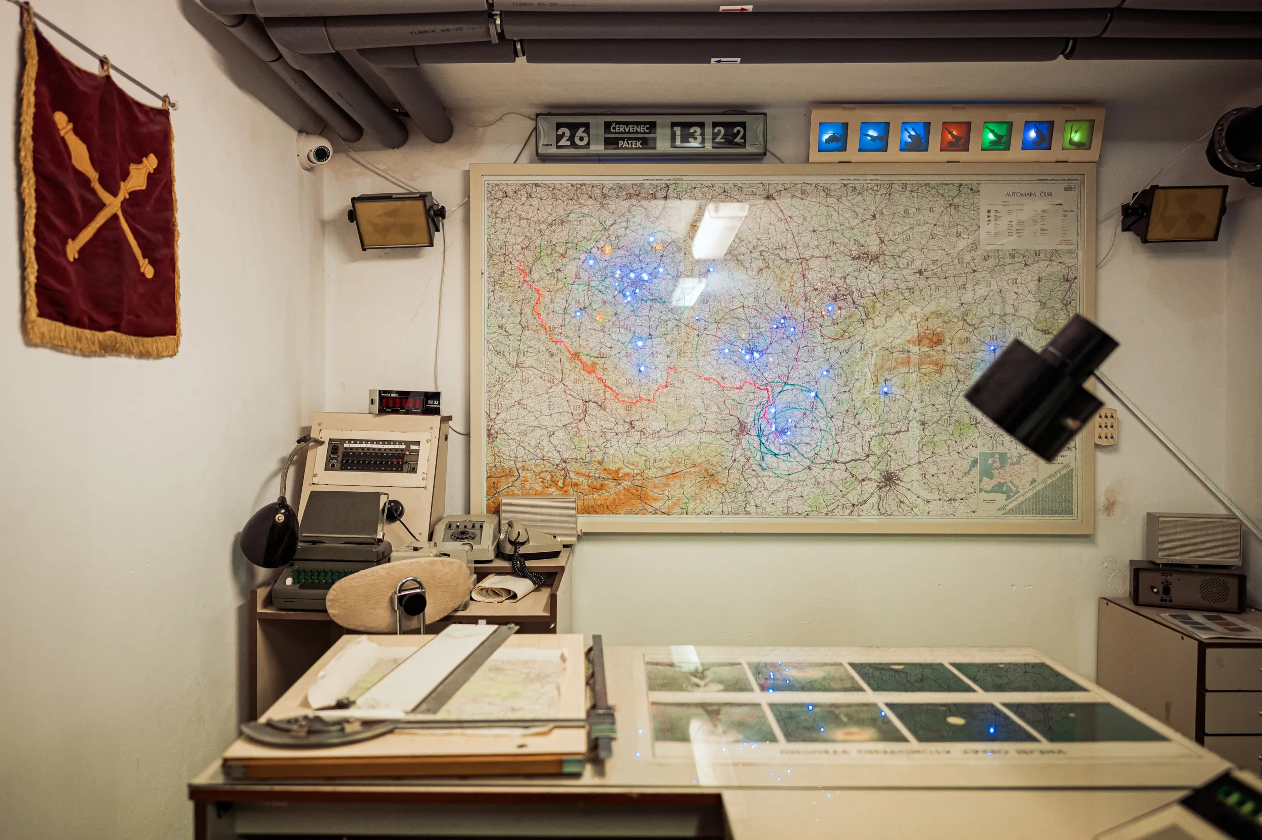 A large map with blue and red markings on a wall, surrounded by vintage equipment and a red banner with a gold emblem