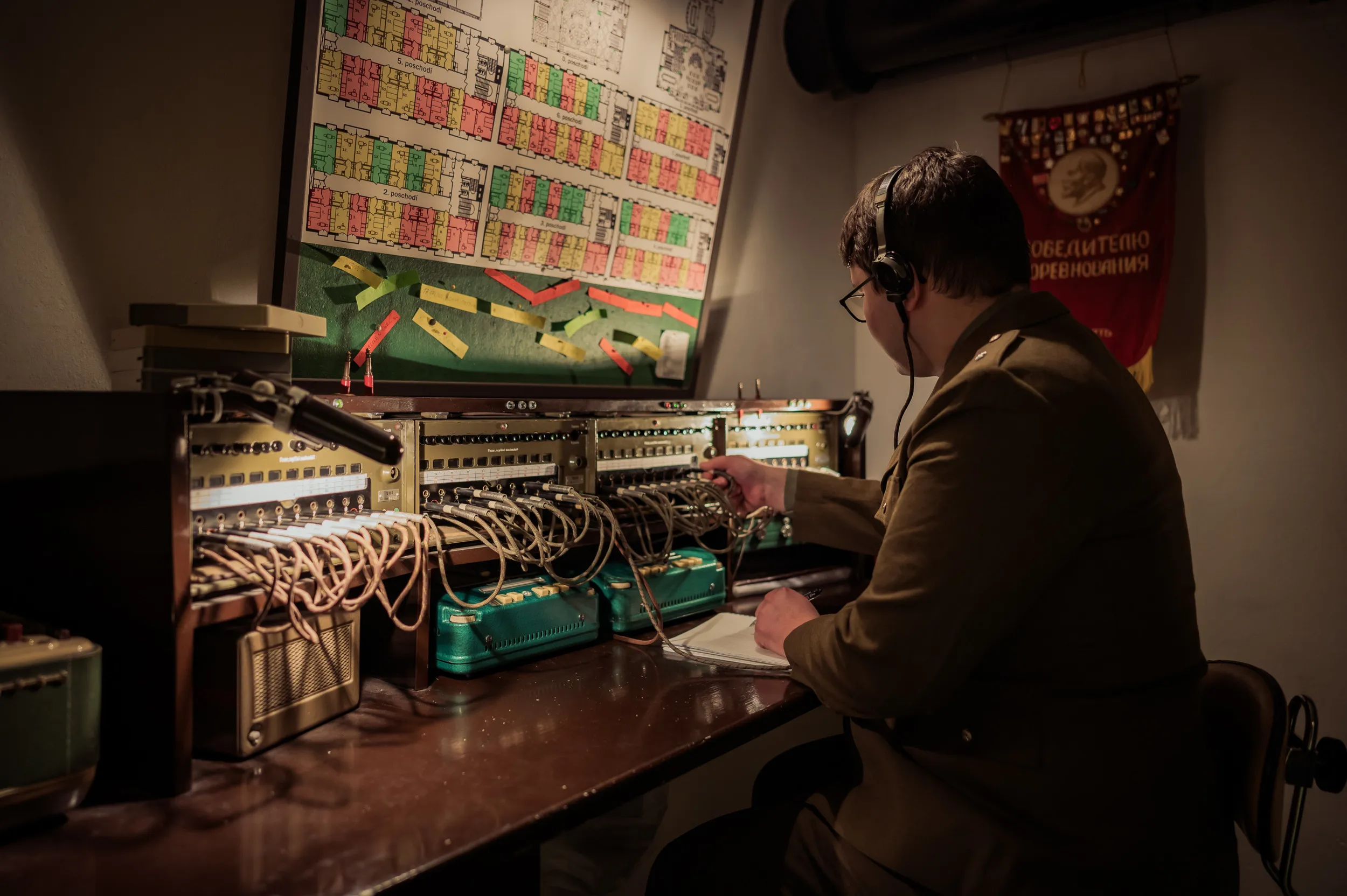 Person in uniform operating vintage communication equipment with a chart and banner in the background