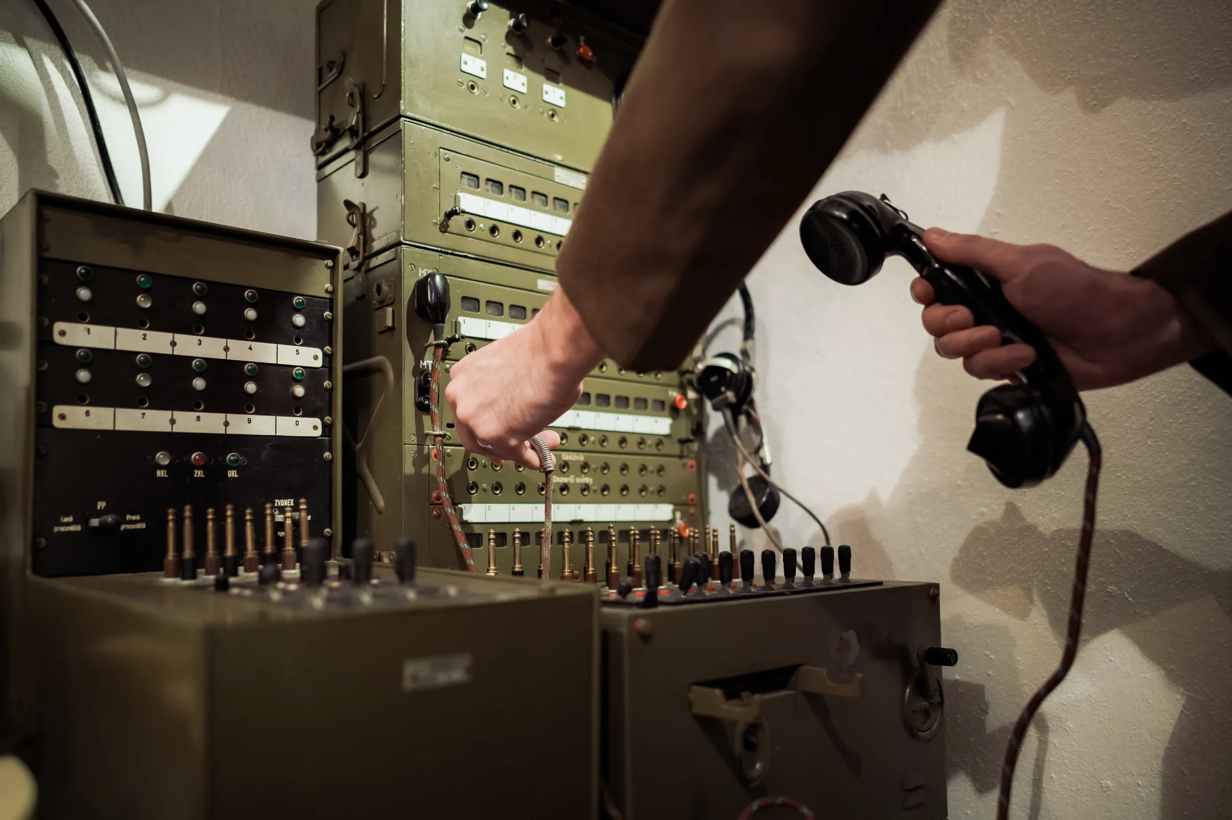 Hands operating a vintage military communication panel with switches and a telephone receiver
