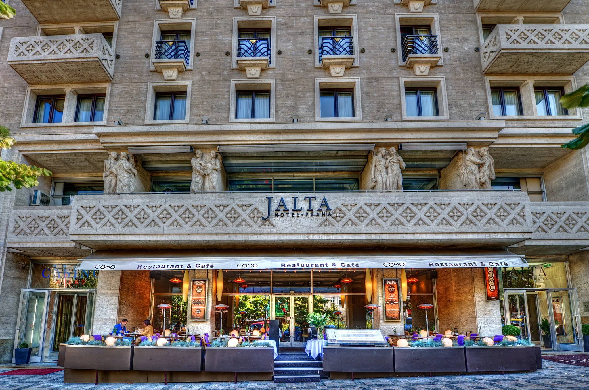 Exterior of Hotel Jalta with 'JALTA' sign above the entrance, featuring classical architecture and outdoor seating