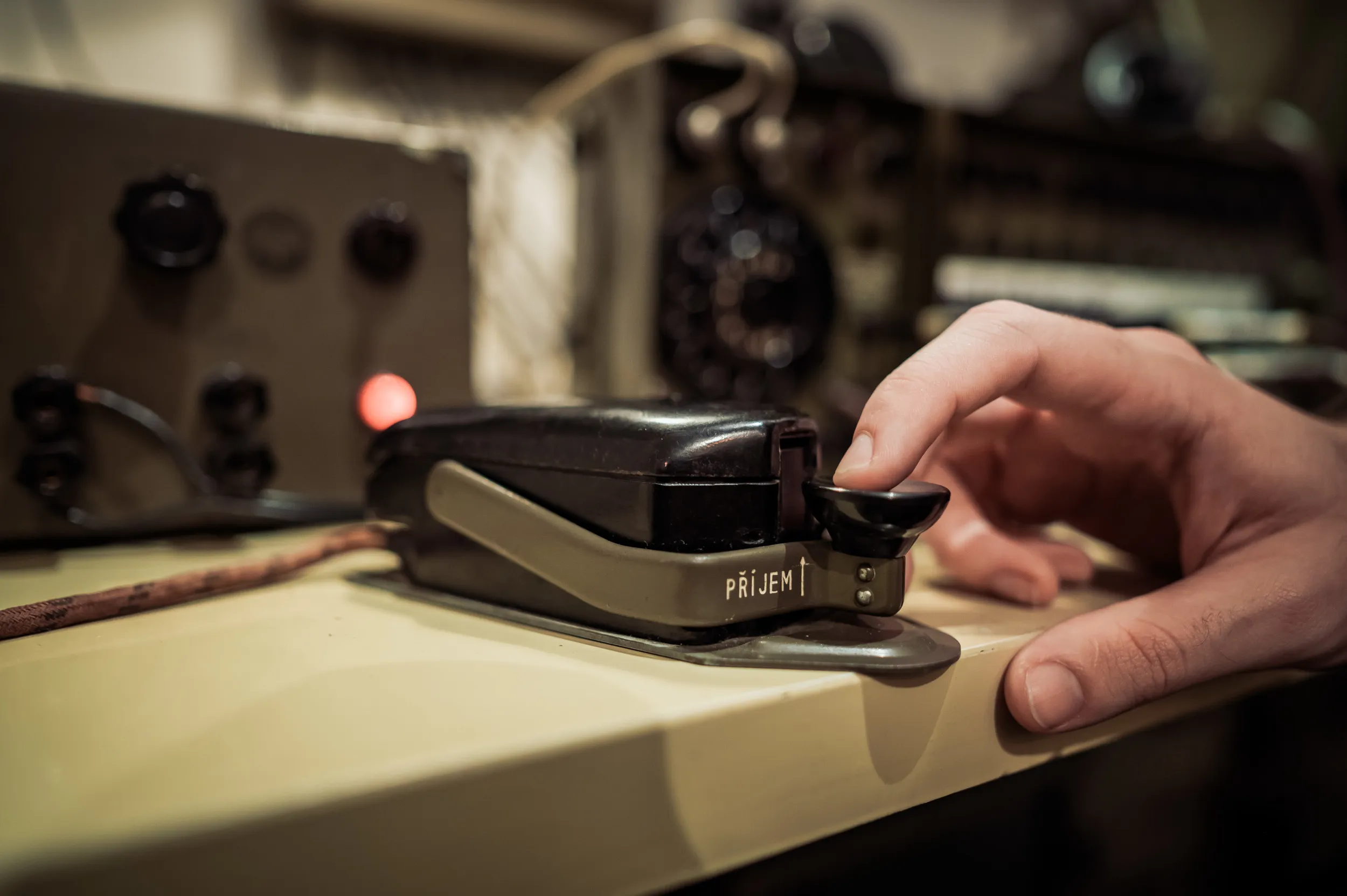 hand operating a vintage communication device labeled 'PŘÍJEM' on a table