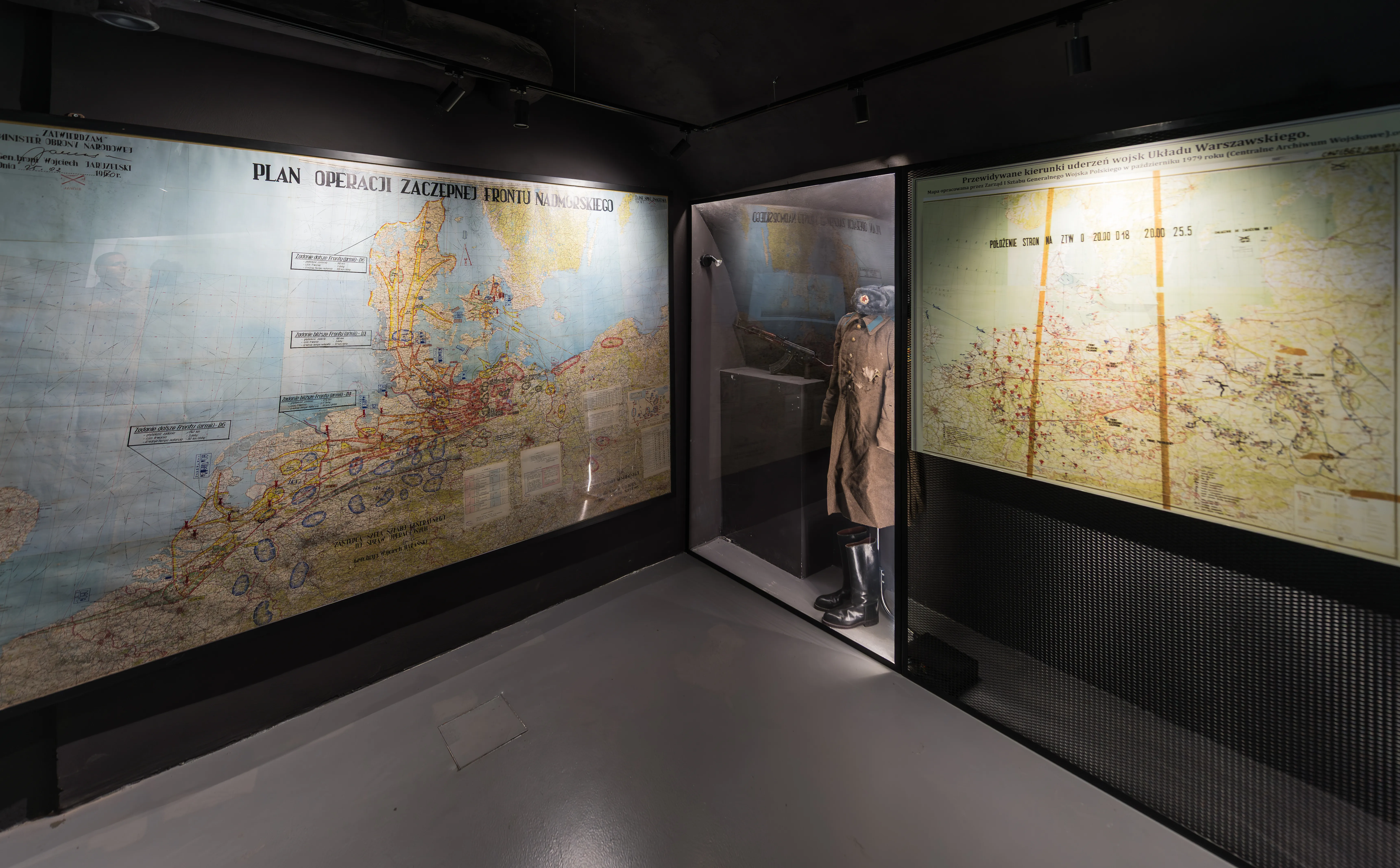 Grandes mapas históricos expuestos en las paredes de una exposición de museo con un maniquí con un abrigo largo