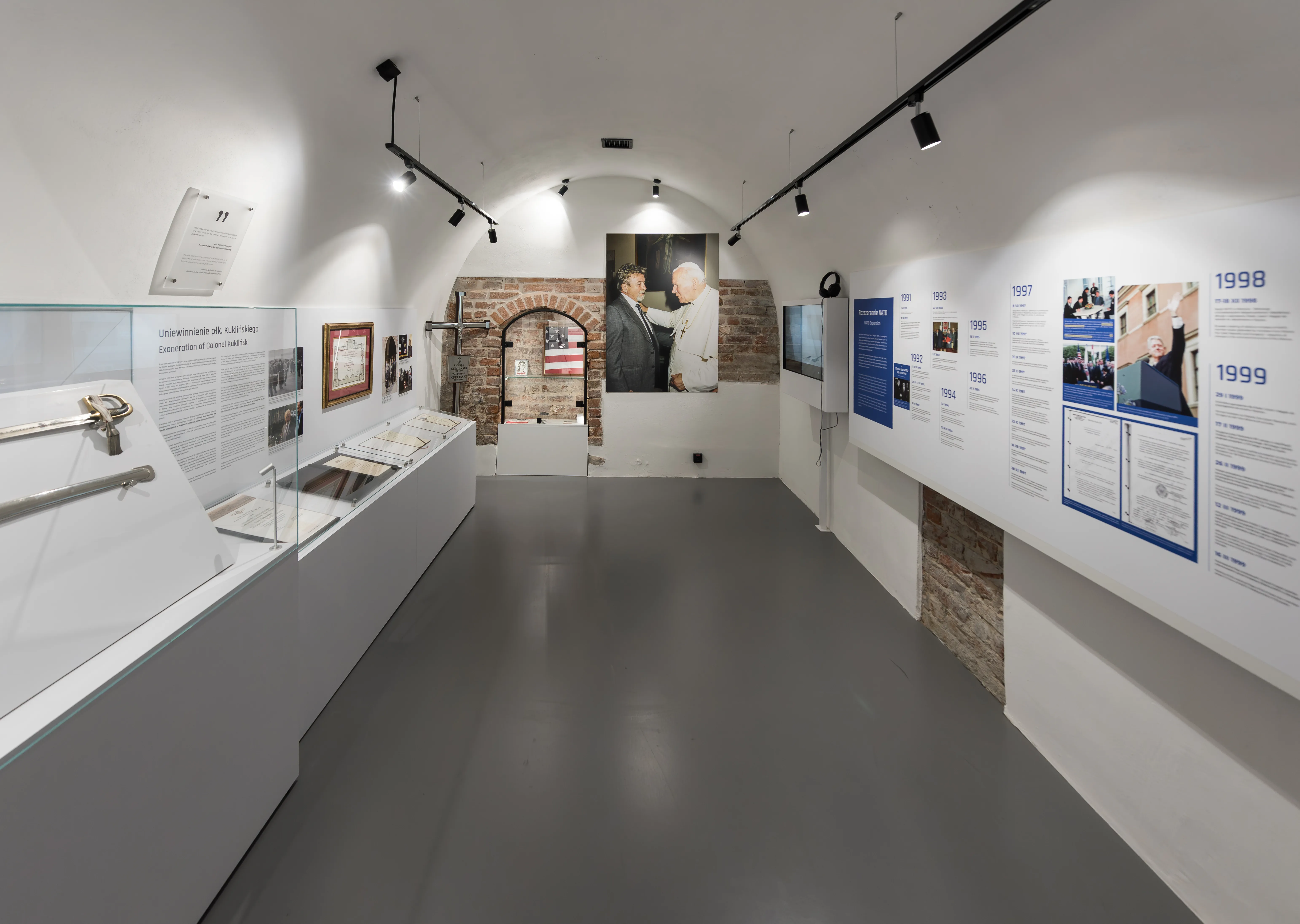 larga galería con paredes blancas, vitrinas y paneles informativos en un museo