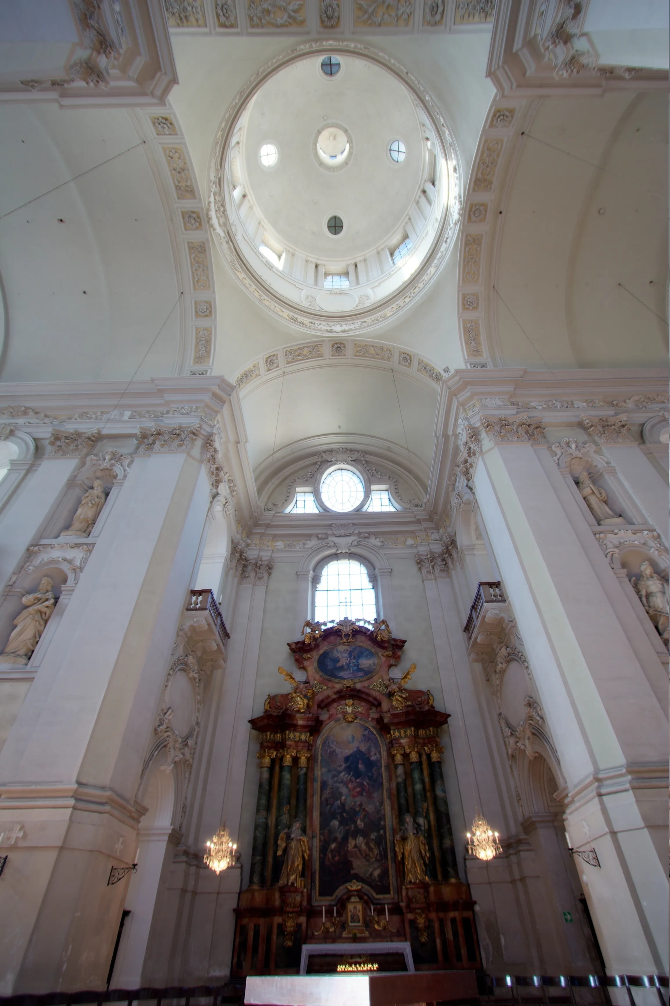 Vista hacia arriba del interior barroco blanco de la iglesia universitaria de Salzburgo, con una gran cúpula y un altar ornamentado.