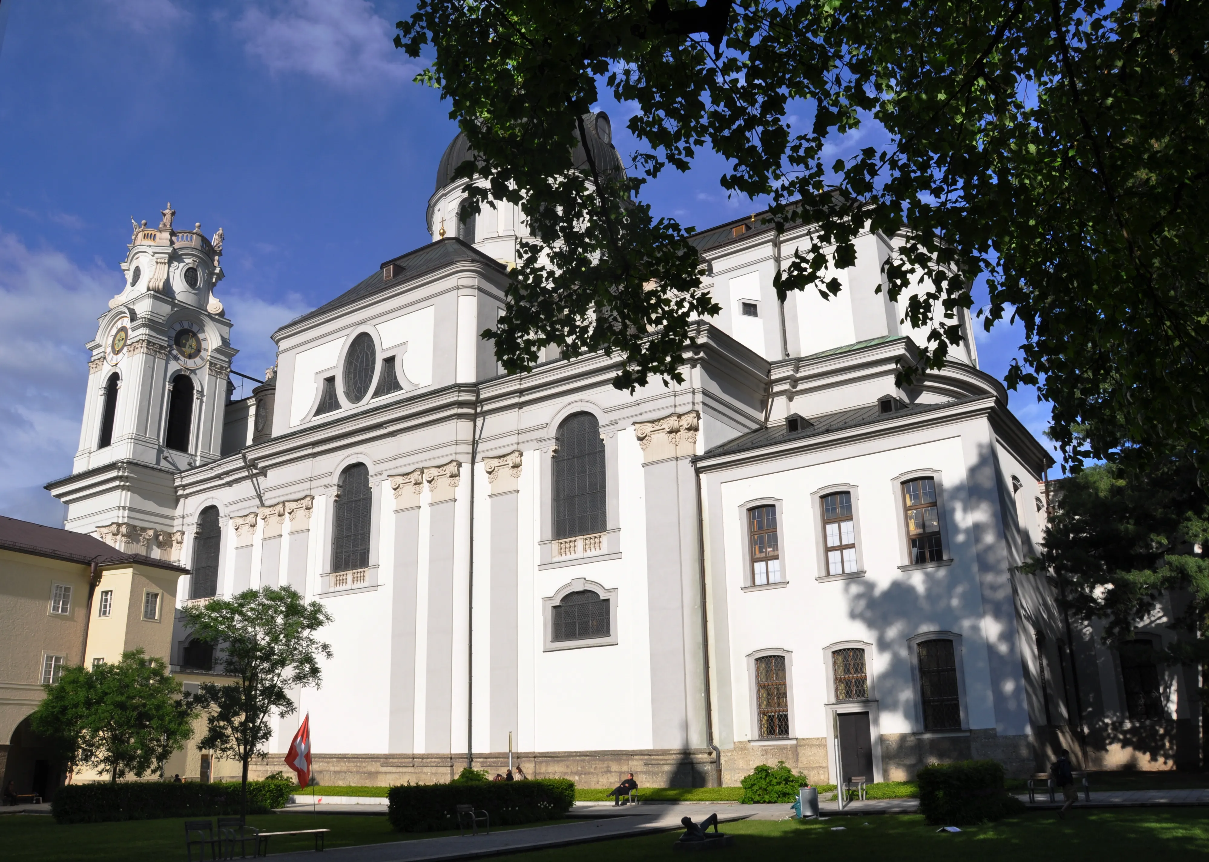 Iglesia colegiata barroca blanca en Salzburgo con torre alta, ventanas arqueadas y fachada curva enmarcada por árboles verdes bajo un cielo azul