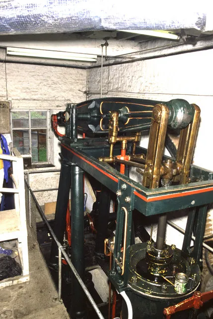 Máquina de vapor victoriana de color verde y latón con adornos rojos dentro de una sala industrial de paredes blancas en Combe Mill.