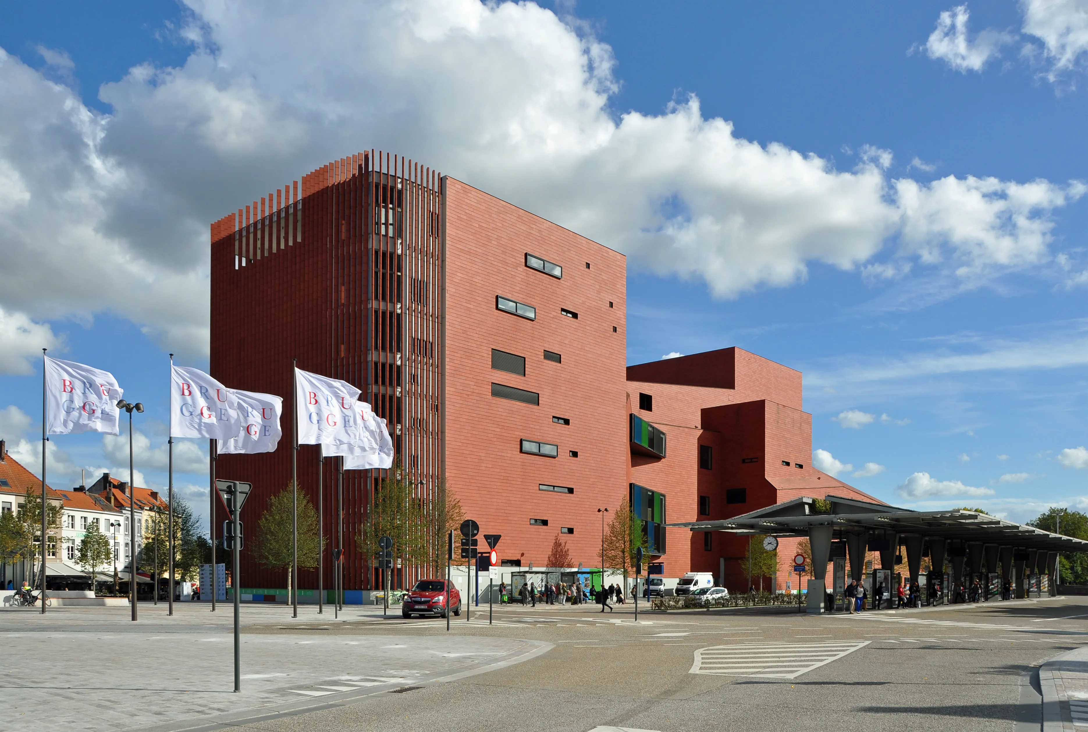 Edificio de ladrillo rojo del Concertgebouw en Brujas con banderas blancas en la plaza frente al edificio bajo un cielo azul con nubes