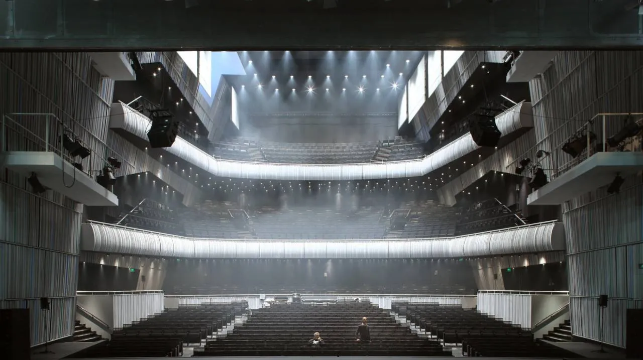 Vista panorámica del interior de la sala de conciertos Concertgebouw Brugge, donde se aprecian las gradas, los balcones blancos curvos y las estructuras de iluminación sobre el escenario.