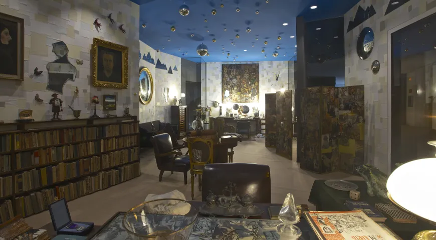Habitación interior con techo azul, estanterías, arte enmarcado y una mesa estampada
