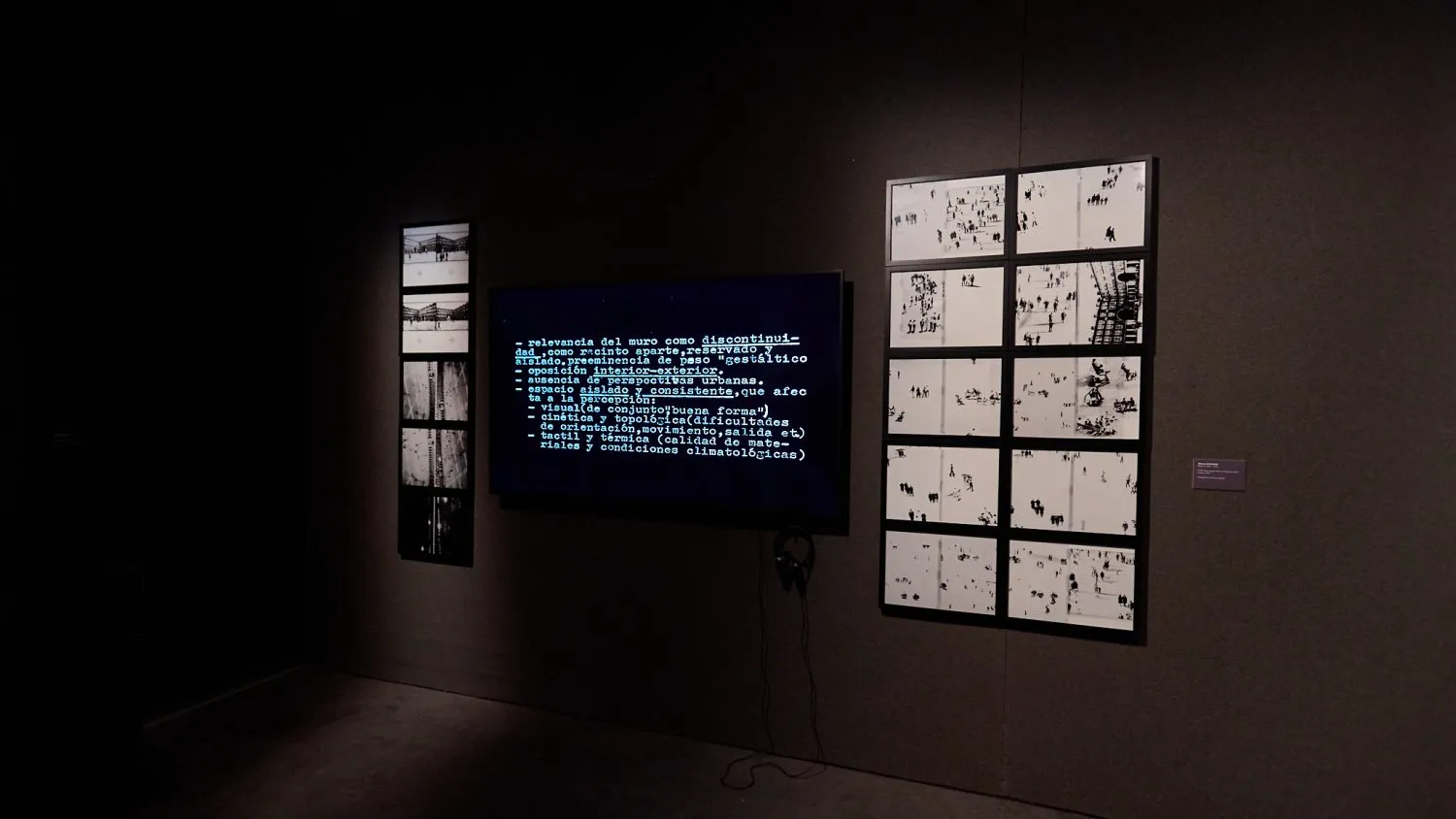 ciemna galeria z centralnym cyfrowym ekranem i dwoma panelami ściennymi wyświetlającymi siatki czarno-białych obrazów