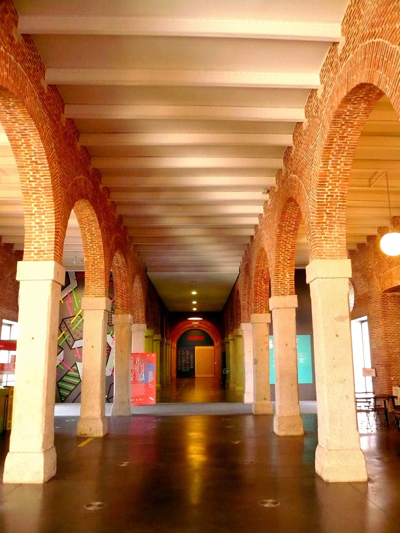 Un largo pasillo con arcos de ladrillo rojo y columnas blancas en el Museo de Arte Contemporáneo Conde Duque