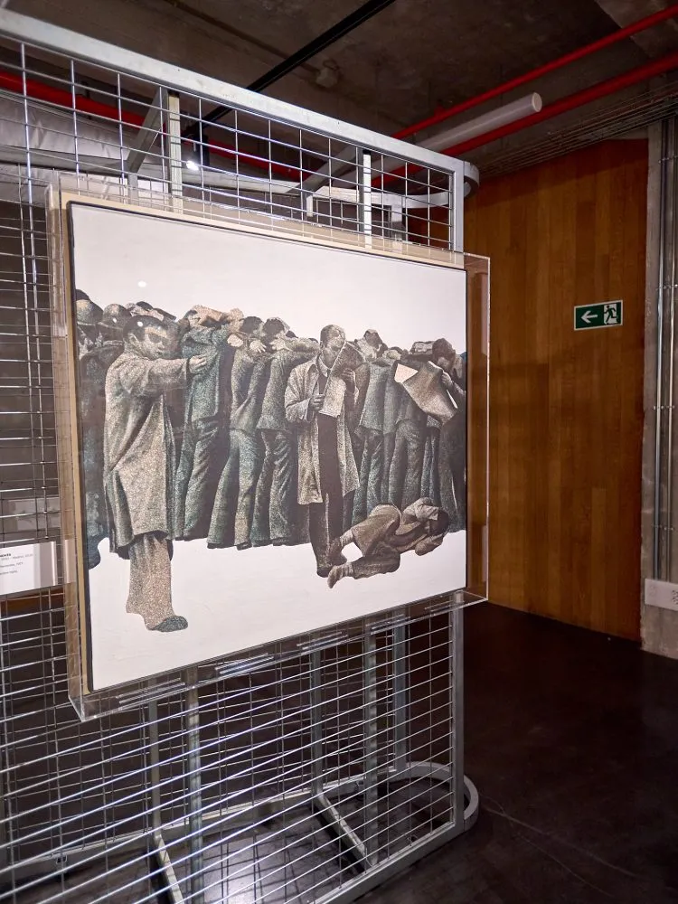 Oprawione dzieło sztuki przedstawiające tłum ludzi w płaszczach, wyeksponowane w metalowej oprawie w galerii.