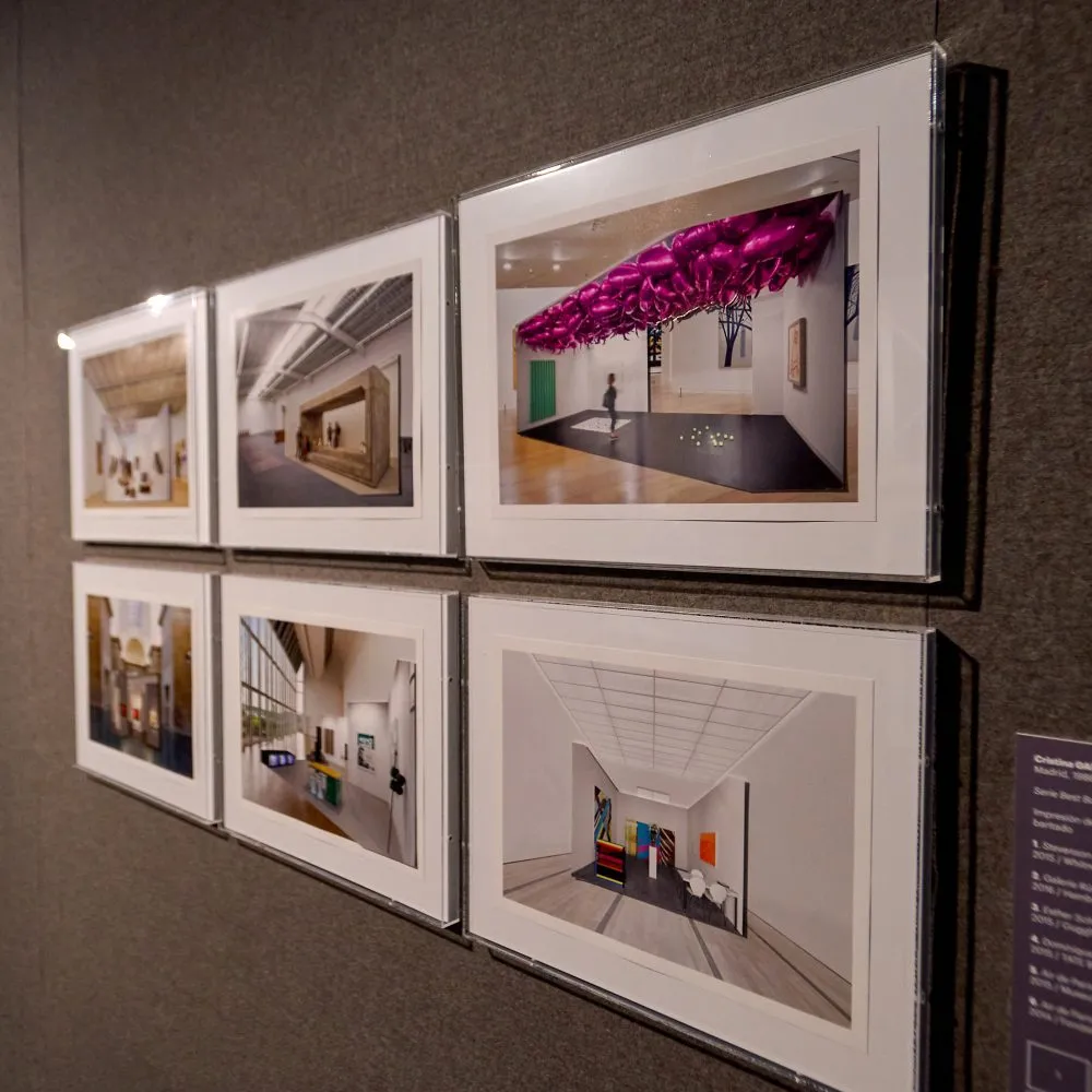 Seis fotografías enmarcadas en una pared que muestran diferentes espacios de galería interiores y una instalación con una escultura de techo morada.