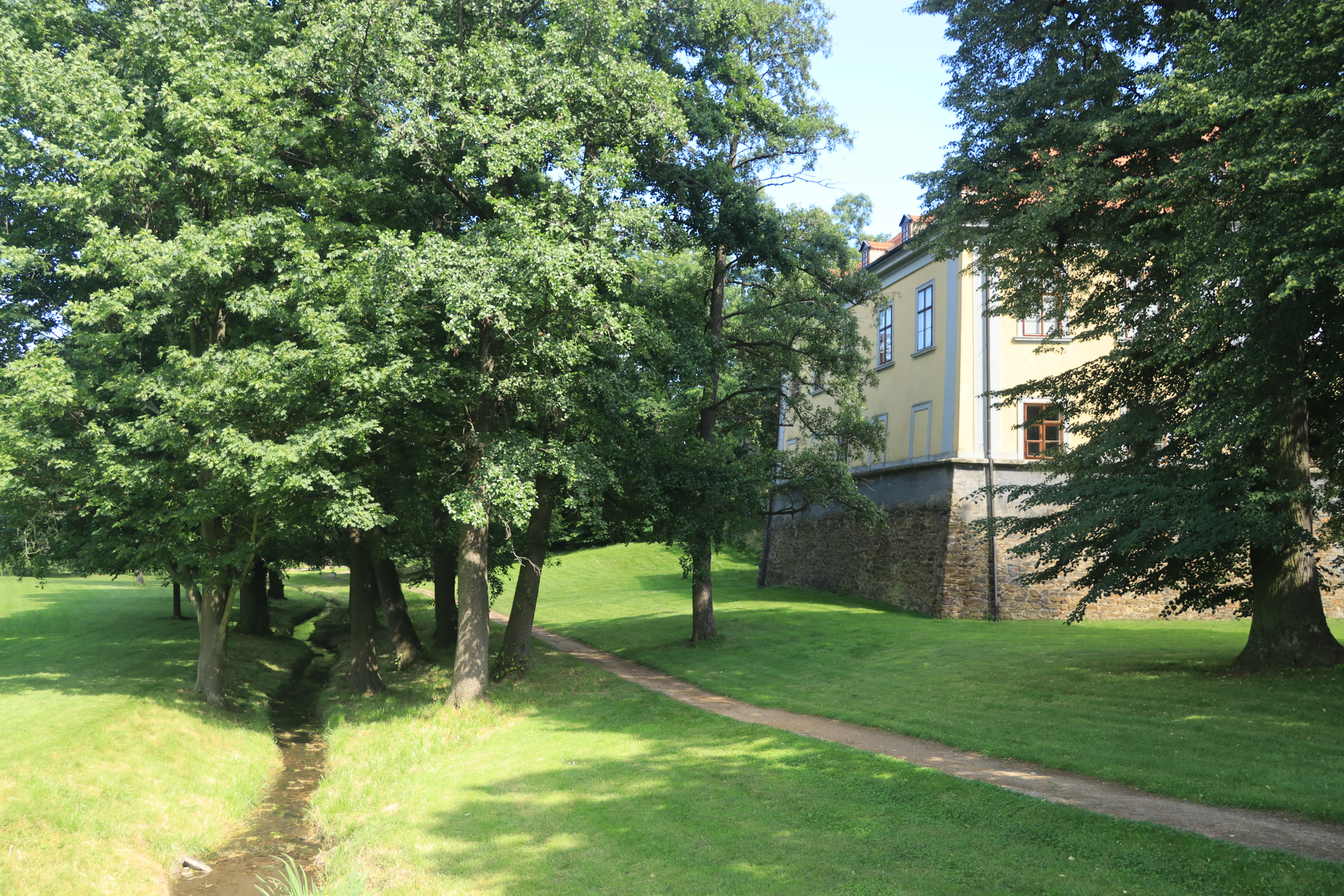Kasteel Ctěnice deels verborgen door bomen met een graspad dat ernaartoe leidt