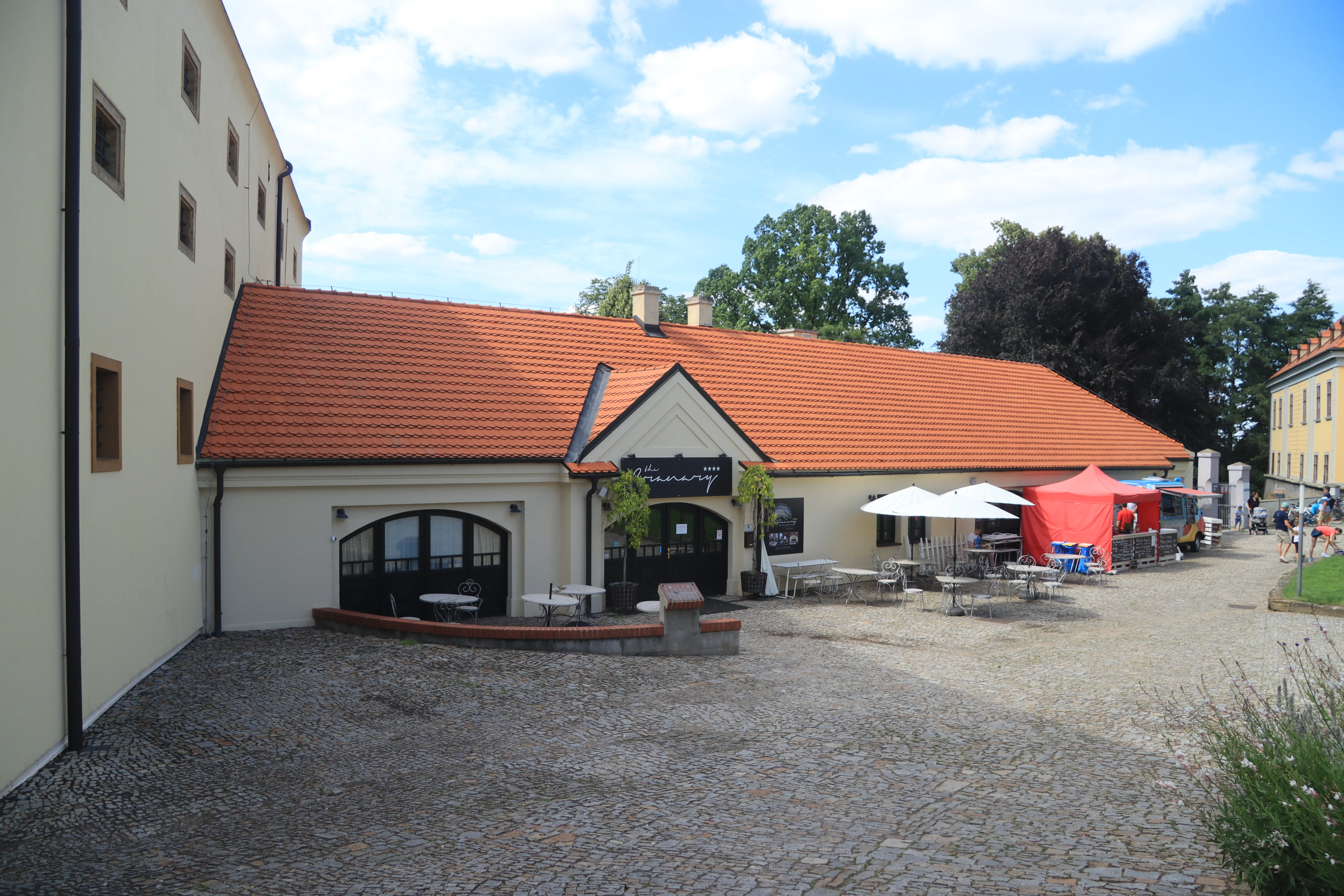 Kasteel binnenplaats van Ctěnice met een gebouw met een rood pannendak, buiten zitplaatsen en een bord voor het kasteel.