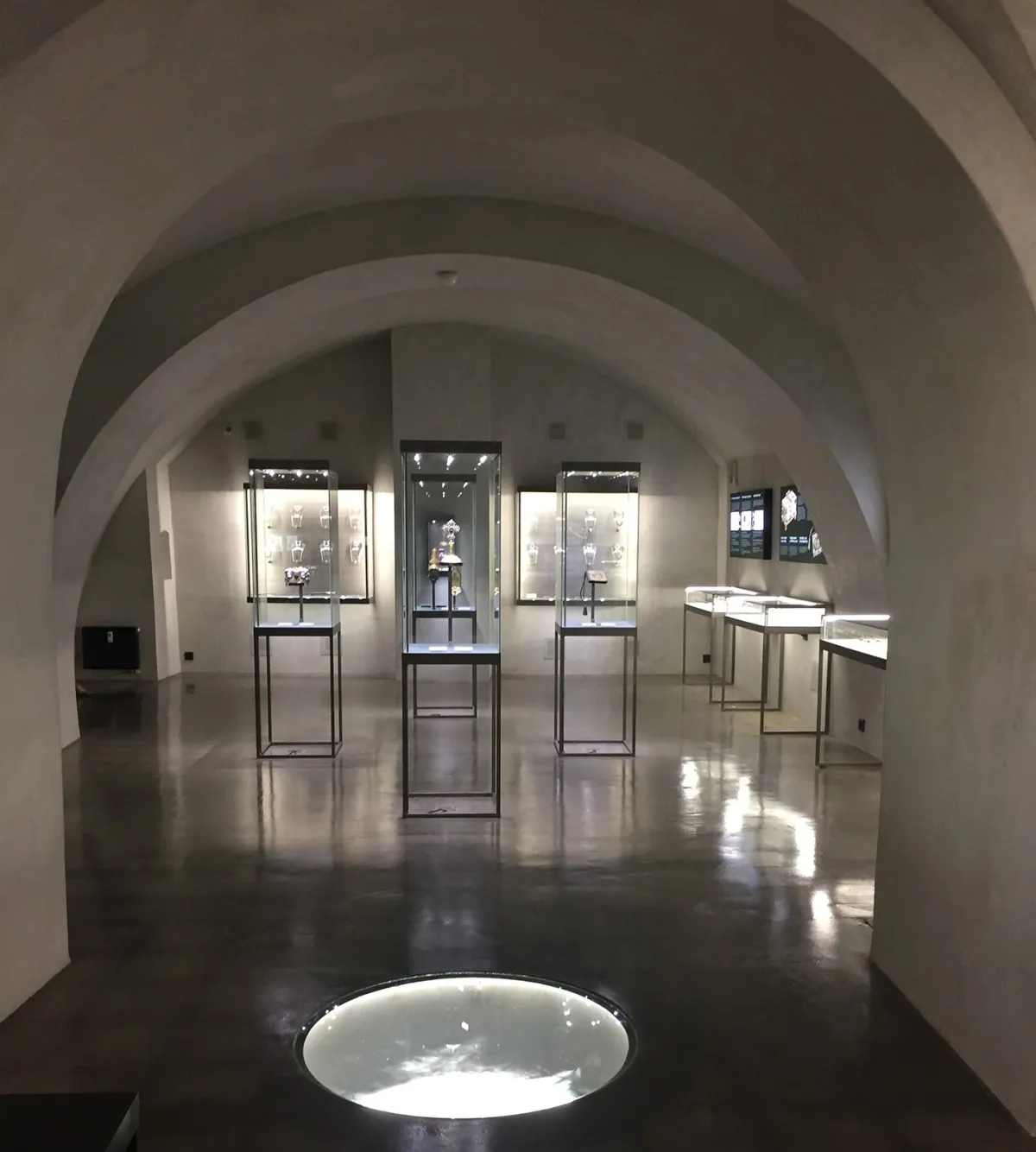 Wnętrze muzeum z łukowatymi sklepieniami, gablotami i okrągłym elementem oświetleniowym na podłodze