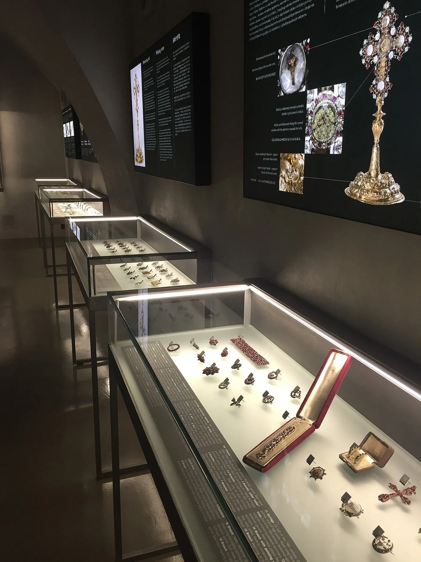 Szklane gabloty zawierające biżuterię i artefakty z elementem czerwonego granatu, oświetlone w galerii muzealnej.