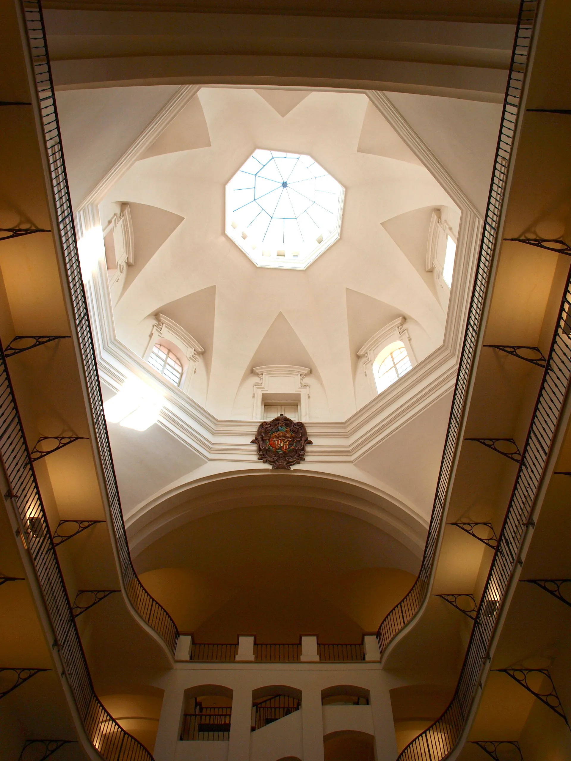 Interieur van een gebouw met een hoog gewelfd plafond, een achthoekige lichtkoepel en balkons met zwarte balustrades.