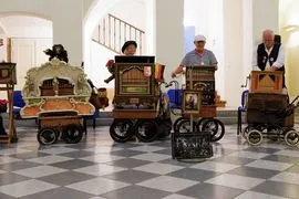Historic musical instruments on display in a museum gallery with a checkered floor