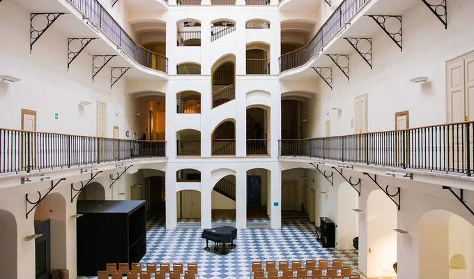 Interieur atrium van het Tsjechisch Muziekmuseum met witte muren, boogvormige deuropeningen, zwarte balustrades en een dambordpatroon vloer