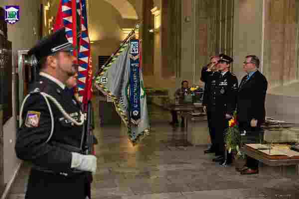 Oficiales de policía uniformados de pie en un salón histórico con banderas y una pancarta ceremonial