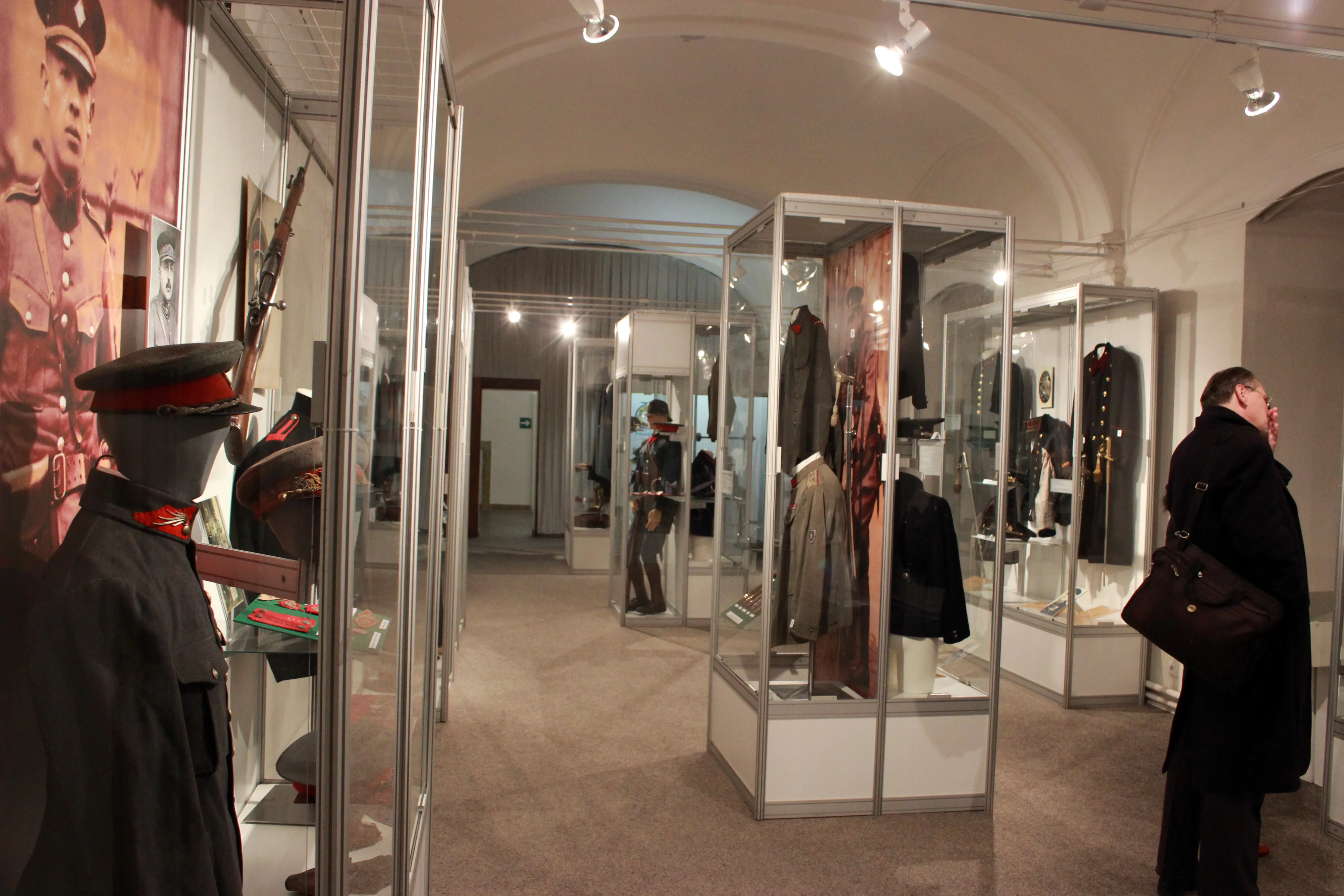 Interior of a museum with glass display cases containing police uniforms and artifacts, a mannequin in a uniform, and visitors in the background