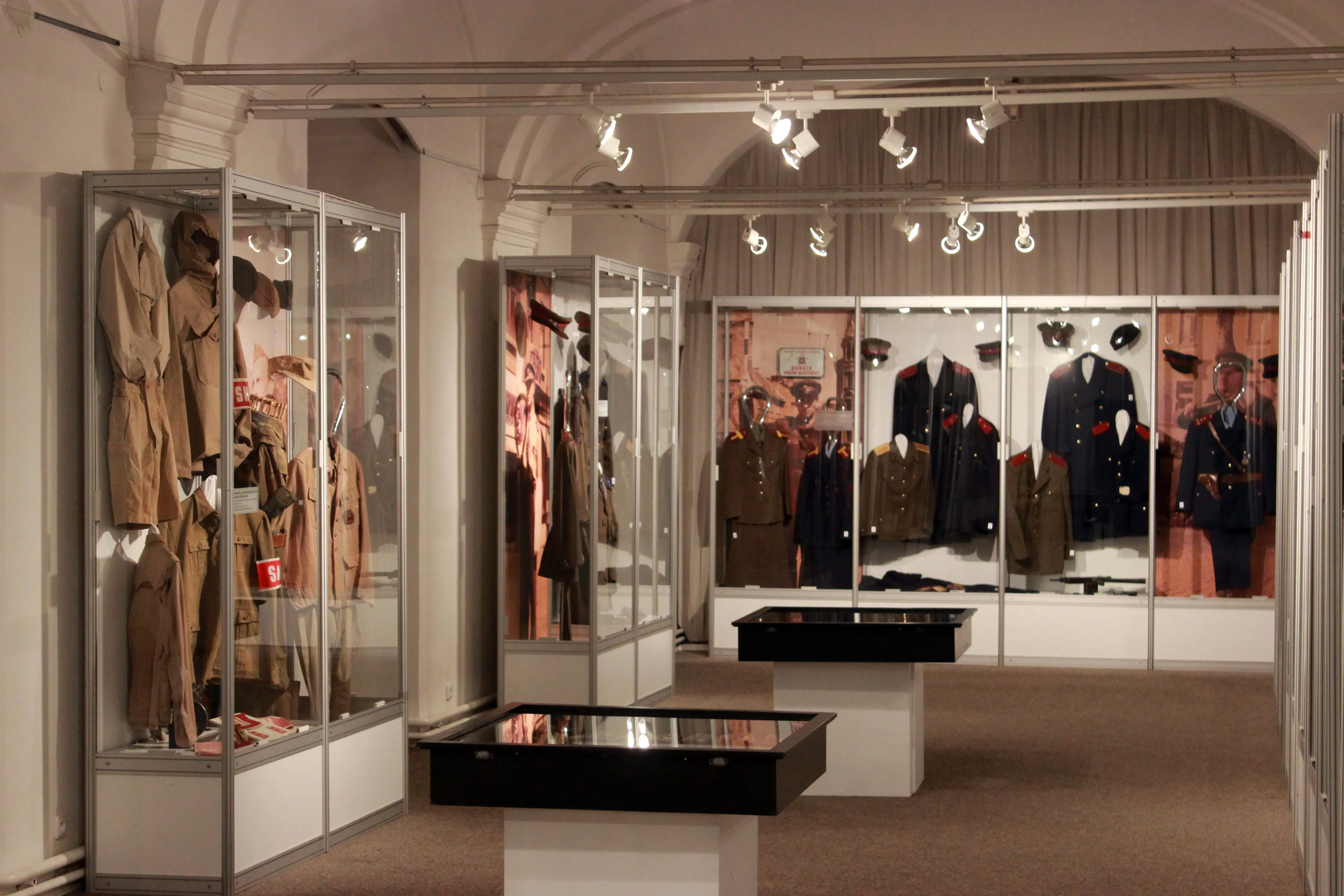 Interior of a museum with glass display cases containing historical police uniforms and artifacts, under track lighting.