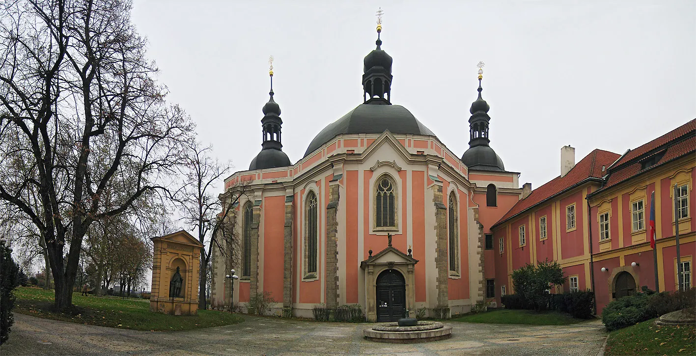 A large historic building with a pink facade, a central dome, and two smaller domes, surrounded by bare trees and a paved courtyard.