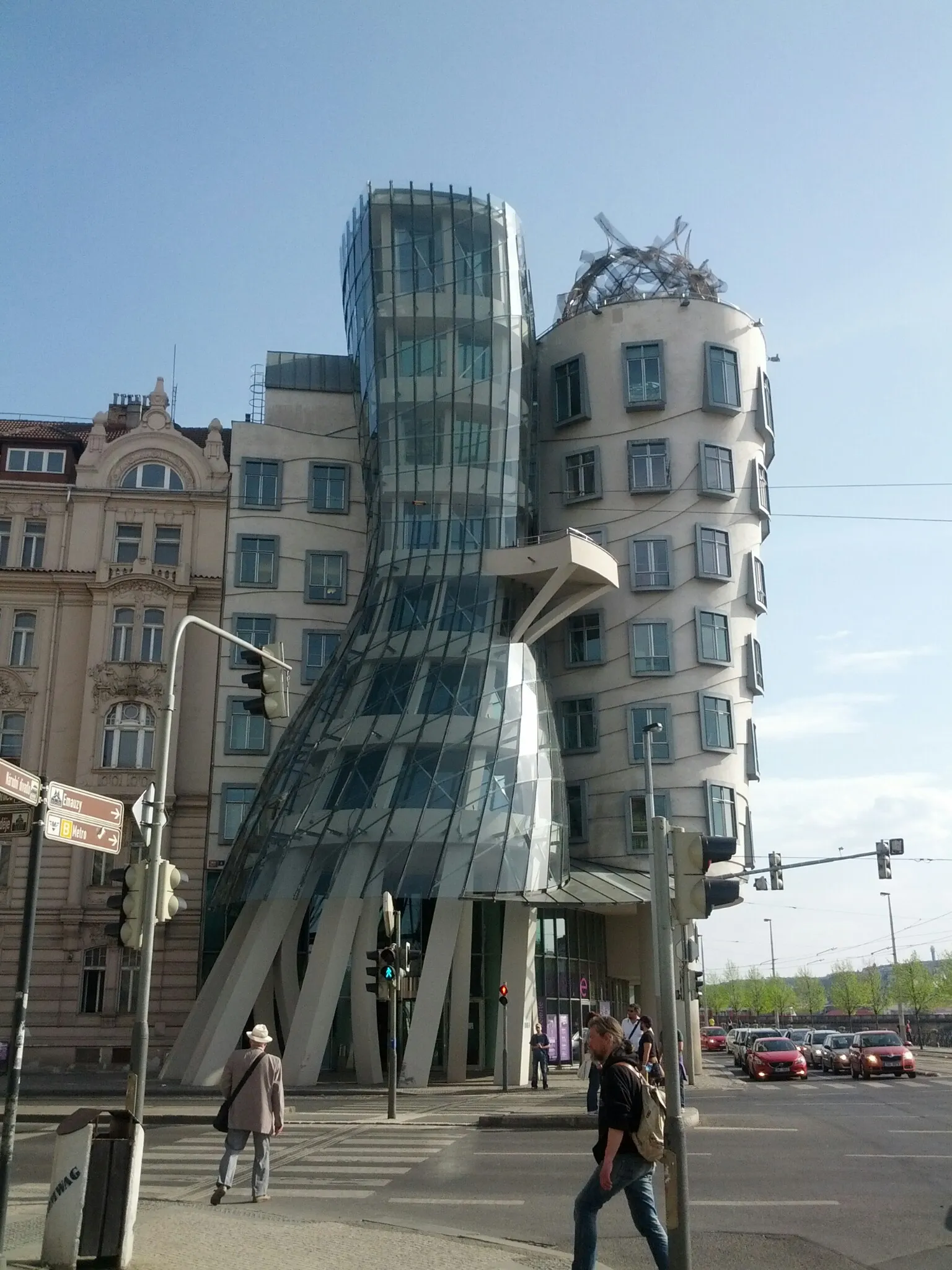 La Casa Danzante, una estructura arquitectónica moderna con fachada de vidrio y una torre blanca curva, ubicada en una calle urbana con peatones y tráfico.