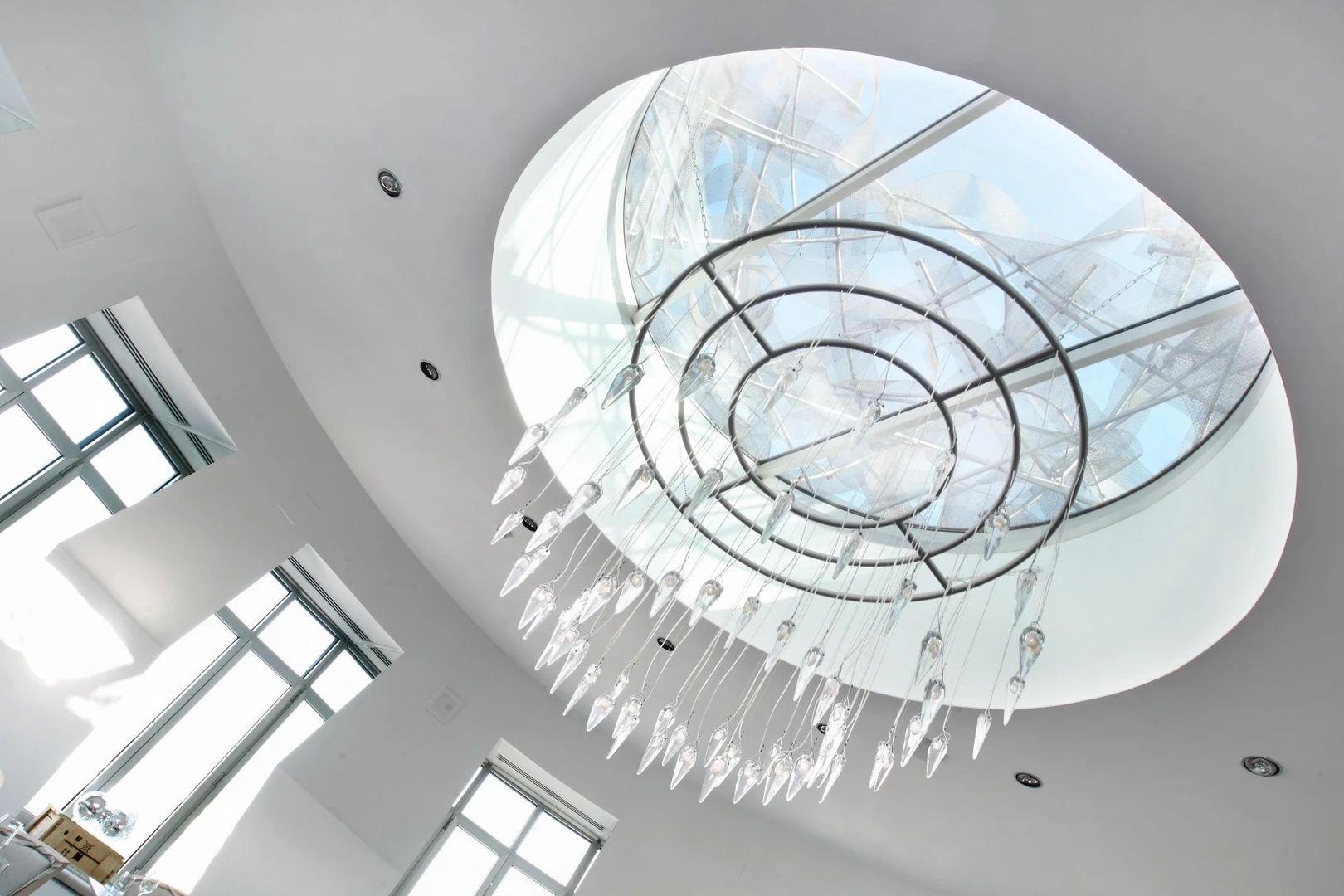 Tragaluz circular con estructura metálica y esculturas de vidrio colgantes dentro de un techo curvo blanco