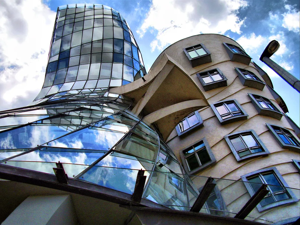Una vista en ángulo bajo de la Casa Danzante, que muestra su distintiva torre de vidrio curvo y estructura de hormigón con ventanas irregulares bajo un cielo nublado.