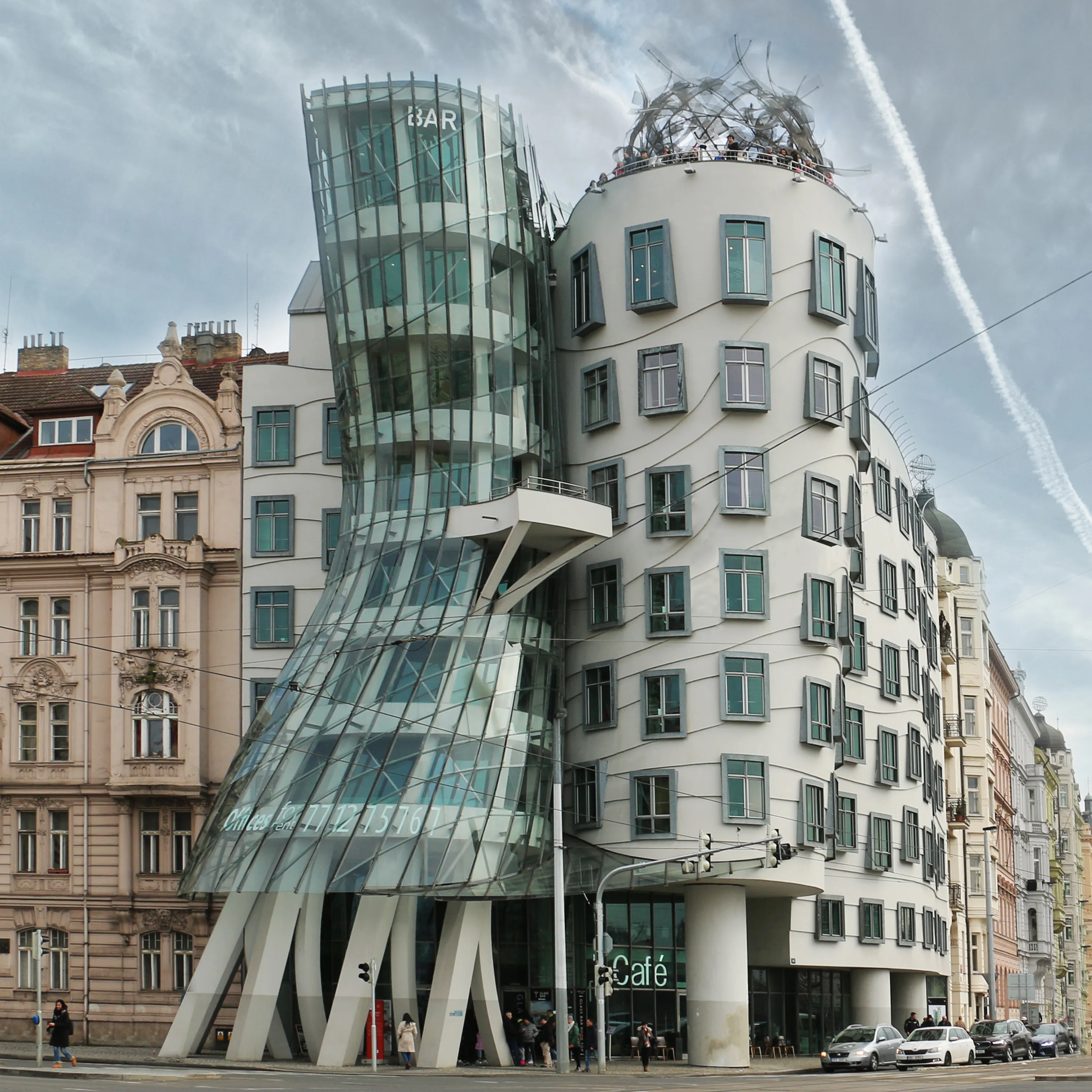 La Casa Danzante, un edificio moderno con fachada de cristal y estructura blanca curvada, situado en una calle de la ciudad con otros edificios al fondo.