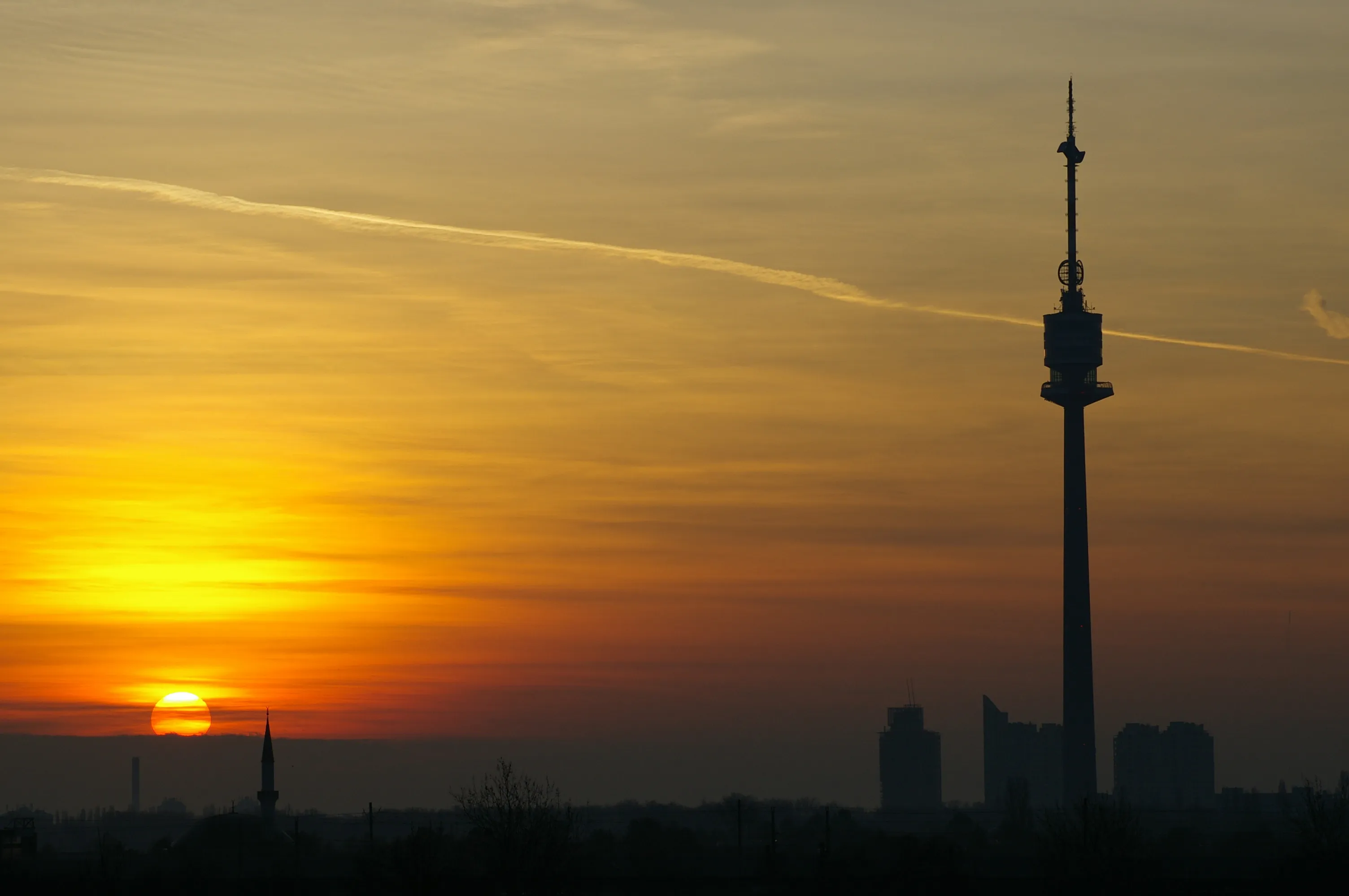 Silhouette of the Danube Tower against a sunset sky with orange and yellow hues