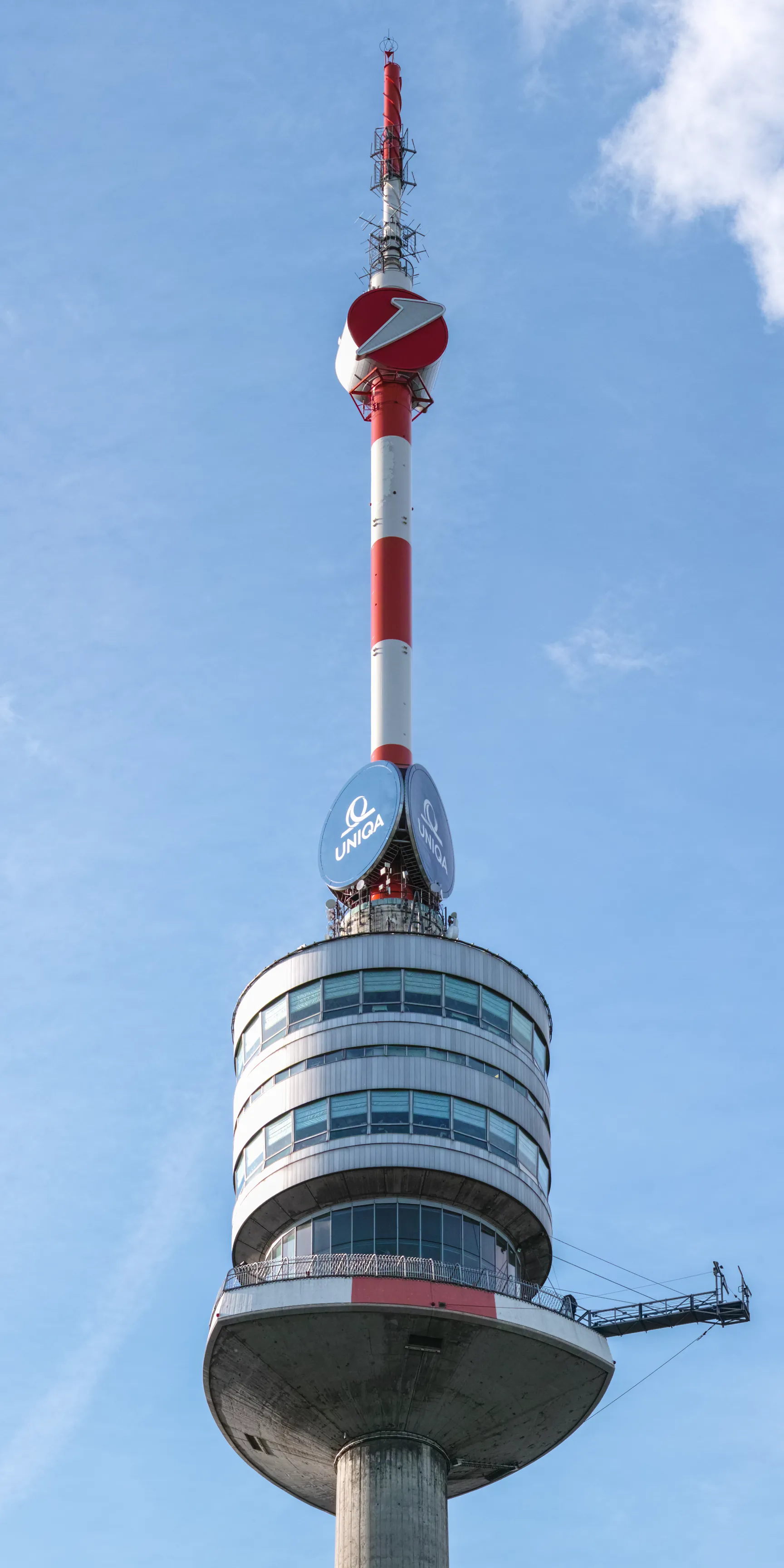 Tall red and white tower with a circular observation deck and a lightning bolt emblem against a blue sky