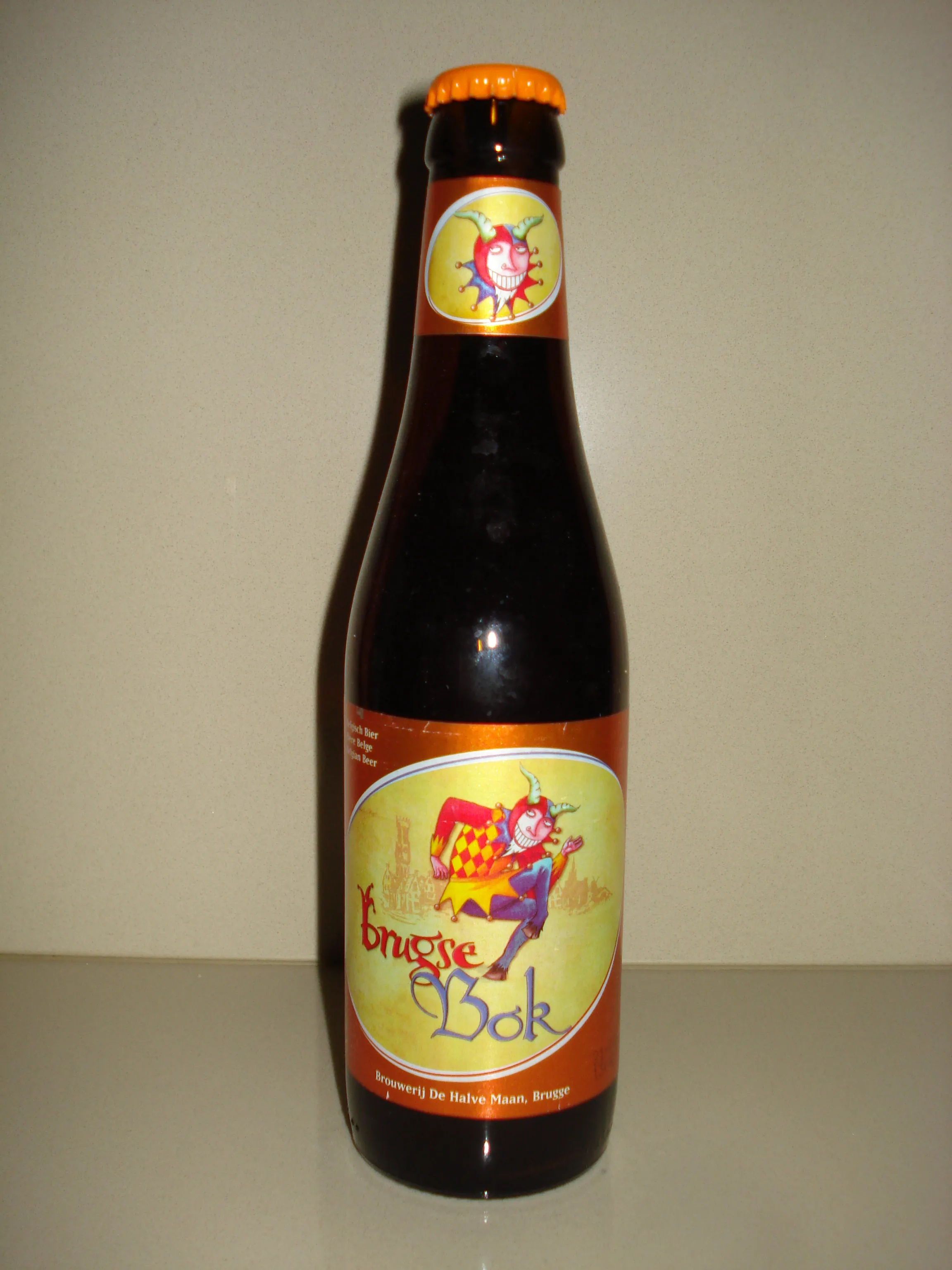 Botella de cristal marrón de cerveza Brugse Bok con tapón naranja y etiqueta colorida de un bufón de Brouwerij De Halve Maan