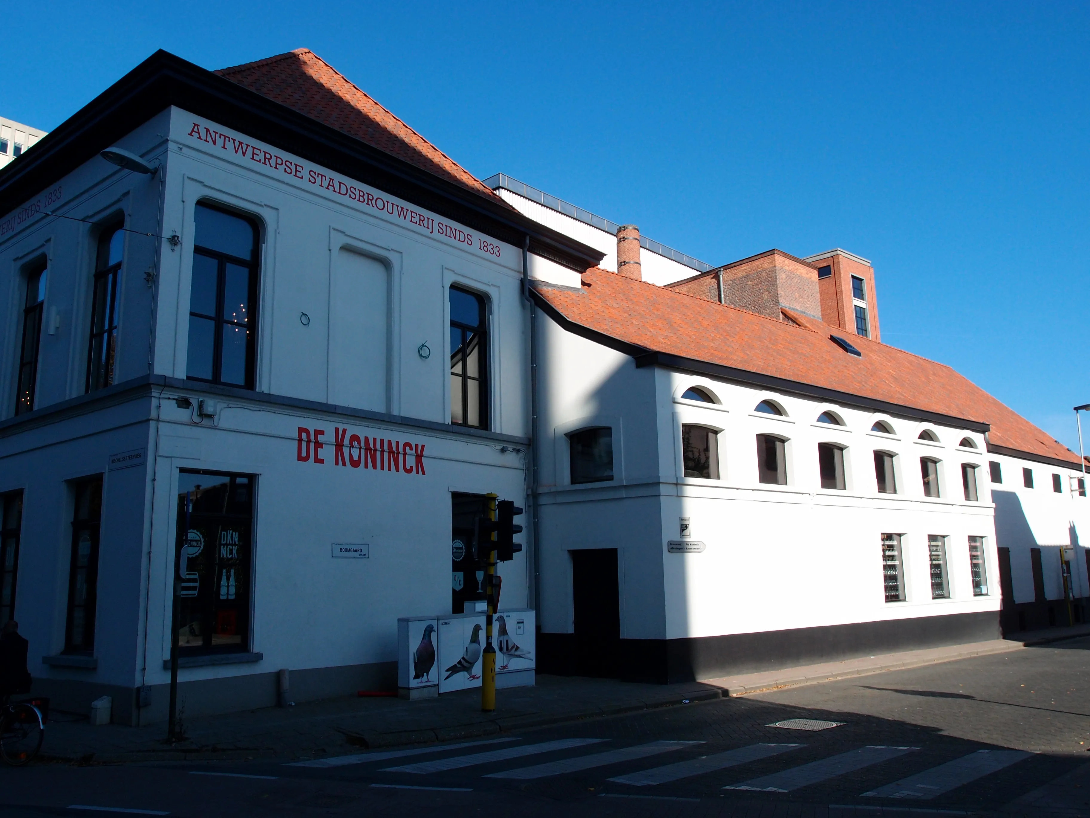 Edificio de la cervecería de color blanco con "DE KONINCK" escrito en letras rojas en la fachada bajo un cielo azul despejado