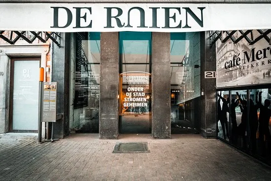 Entrada a nivel de calle de De Ruien con un gran letrero sobre las puertas de cristal, columnas de ladrillo y pavimento de ladrillo en la parte frontal