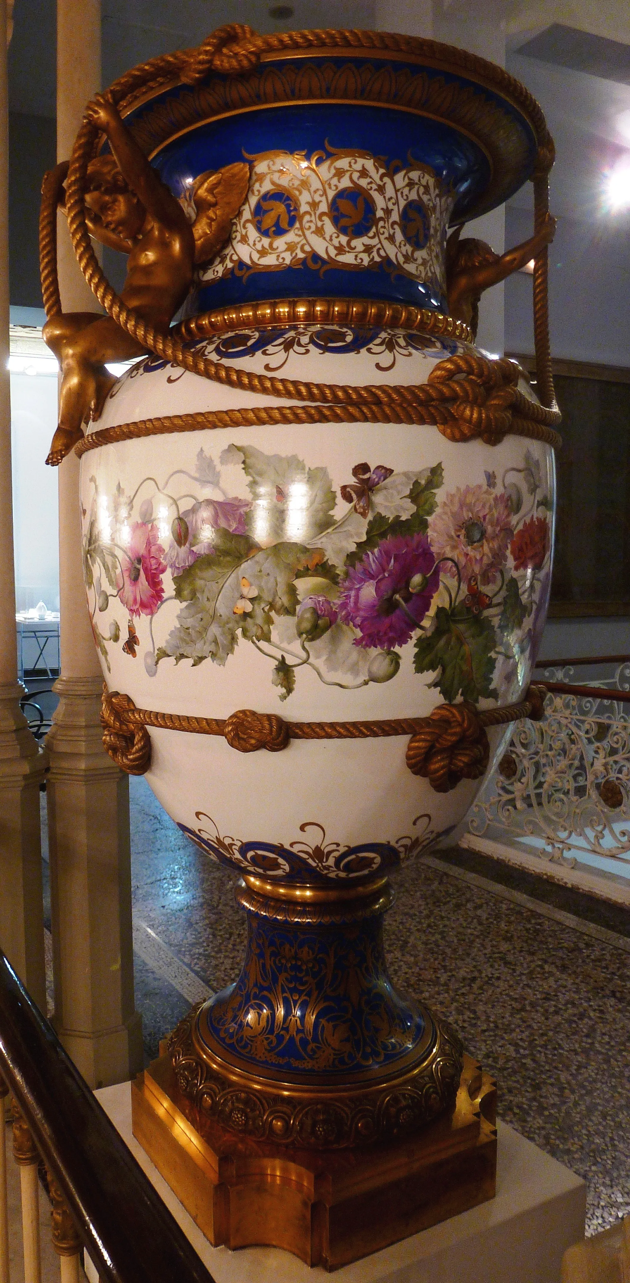 Gran jarrón decorativo con motivos florales y asas doradas expuesto en un museo