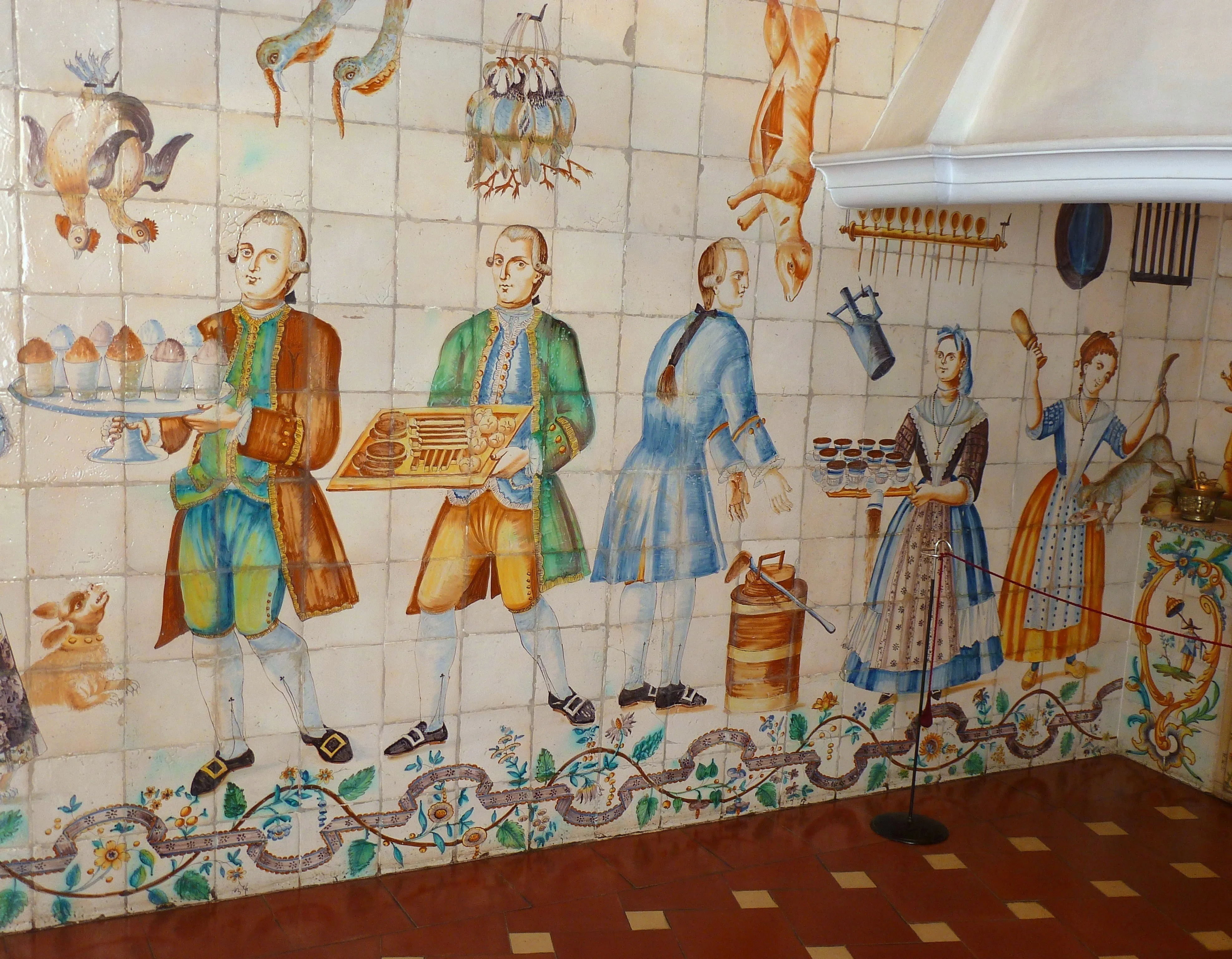 mural de azulejos de colores que muestra figuras históricas con ropa del siglo XVIII, incluyendo un hombre con una bandeja y una mujer con una cesta, sobre una pared de azulejos con patrones decorativos