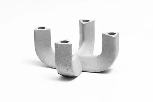 Een witte betonnen kandelaar met een geometrisch design op een wit oppervlak